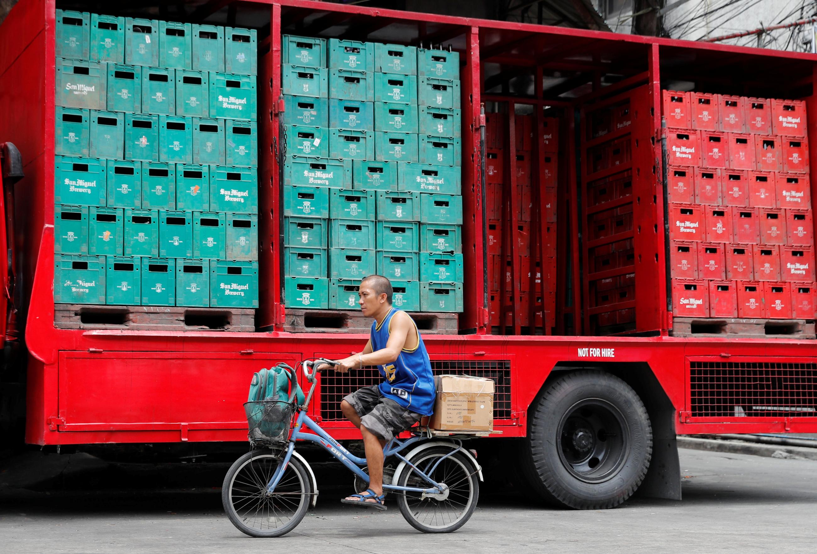 A man cycles past a delivery truck containing crates of San Miguel in Santa Cruz, Manila, Philippines, June 6, 2018. 