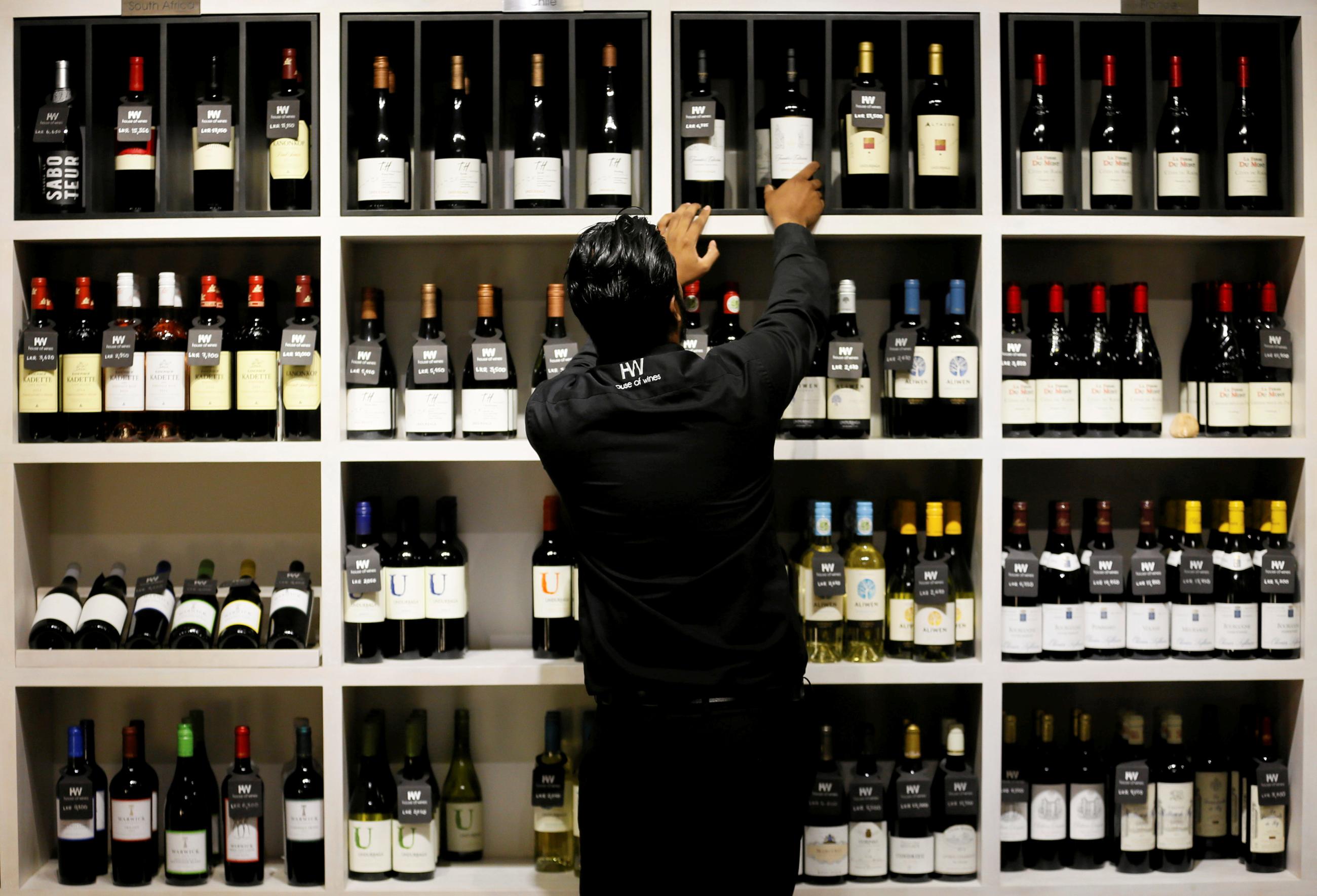A man takes a bottle of wine from a shelf for a customer.