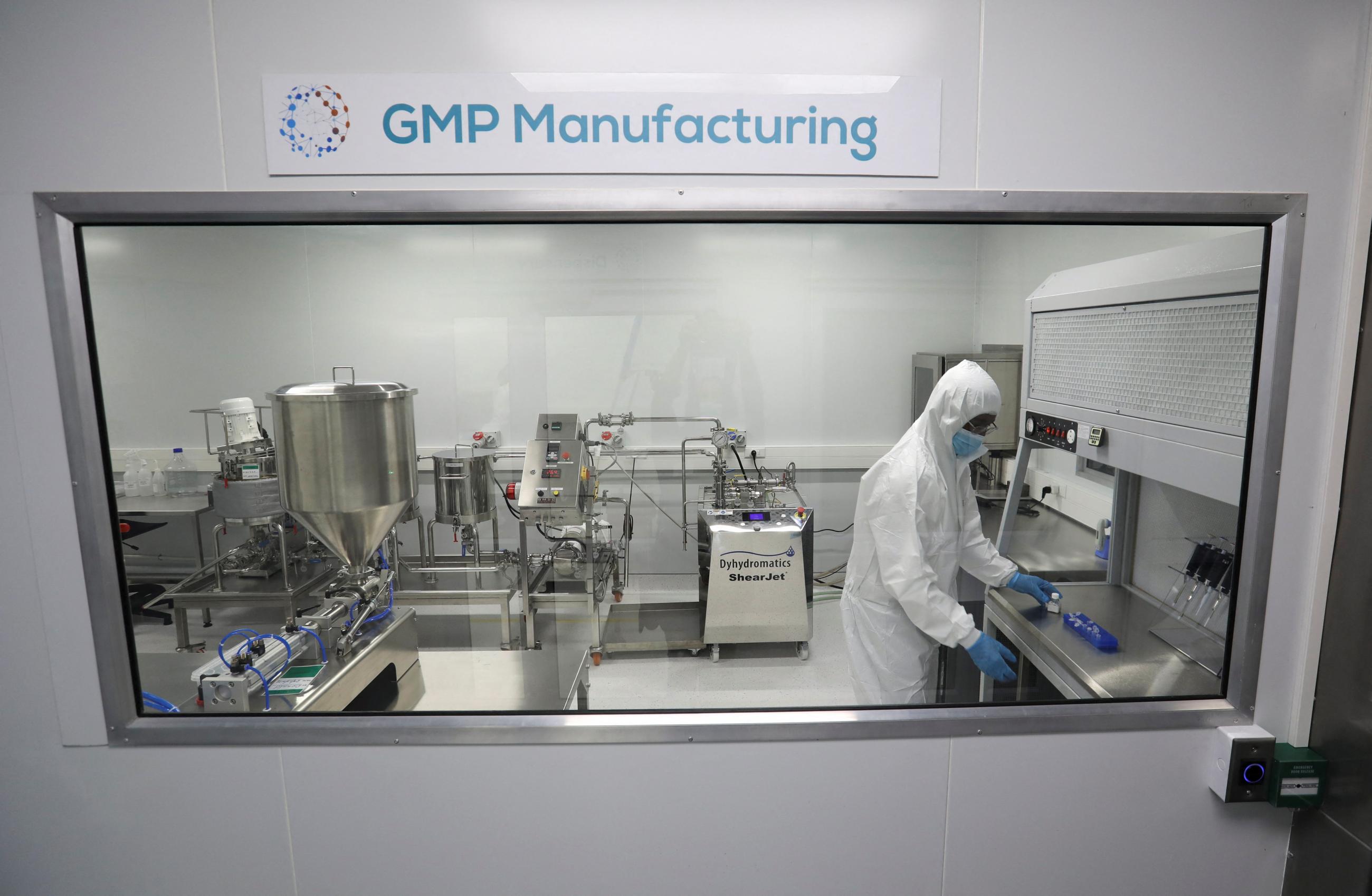 A man in a full protective suit works behind a glass in a lab.