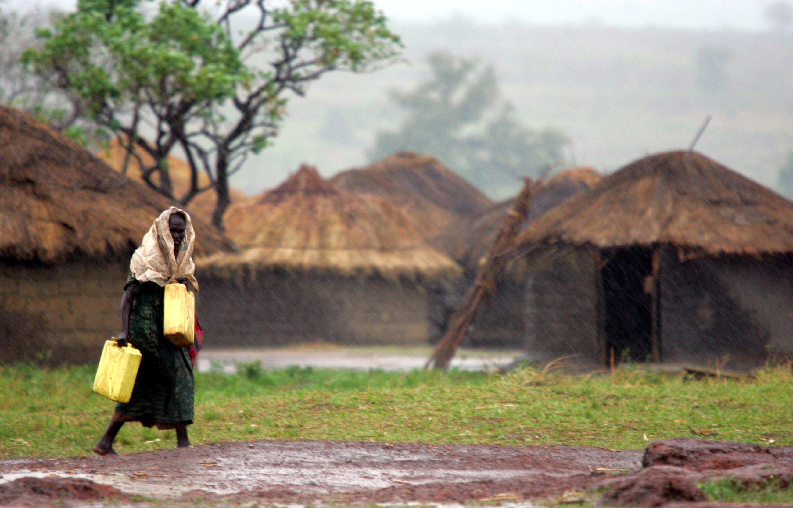 A internally displaced woman walks in the rain to fetch water at Olwal camp.