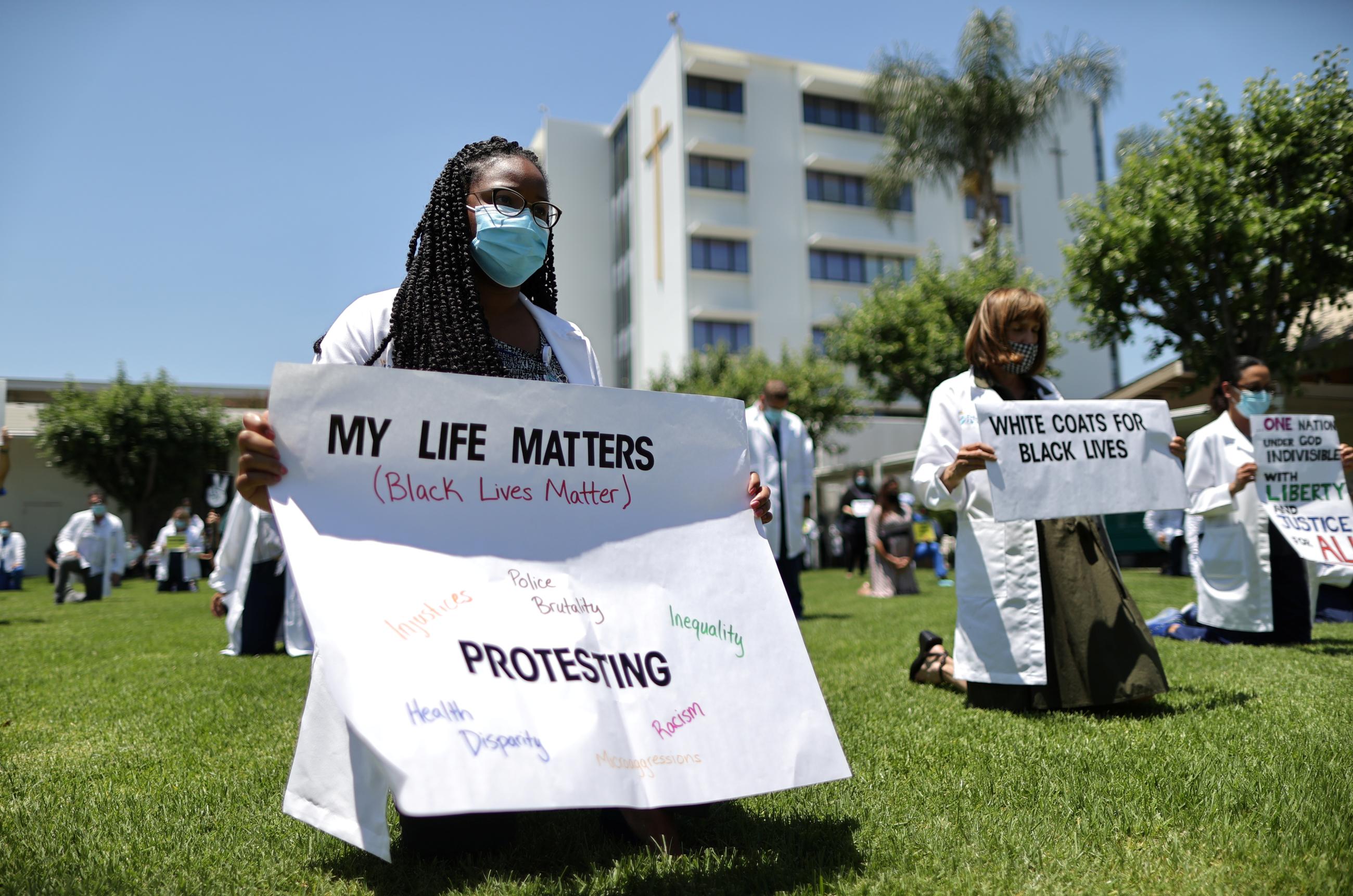 Doctor Jazma Phelps kneels while holding a sign during a "White Coats for Black Lives'' tribute for George Floyd and other African-Americans who died in police custody,