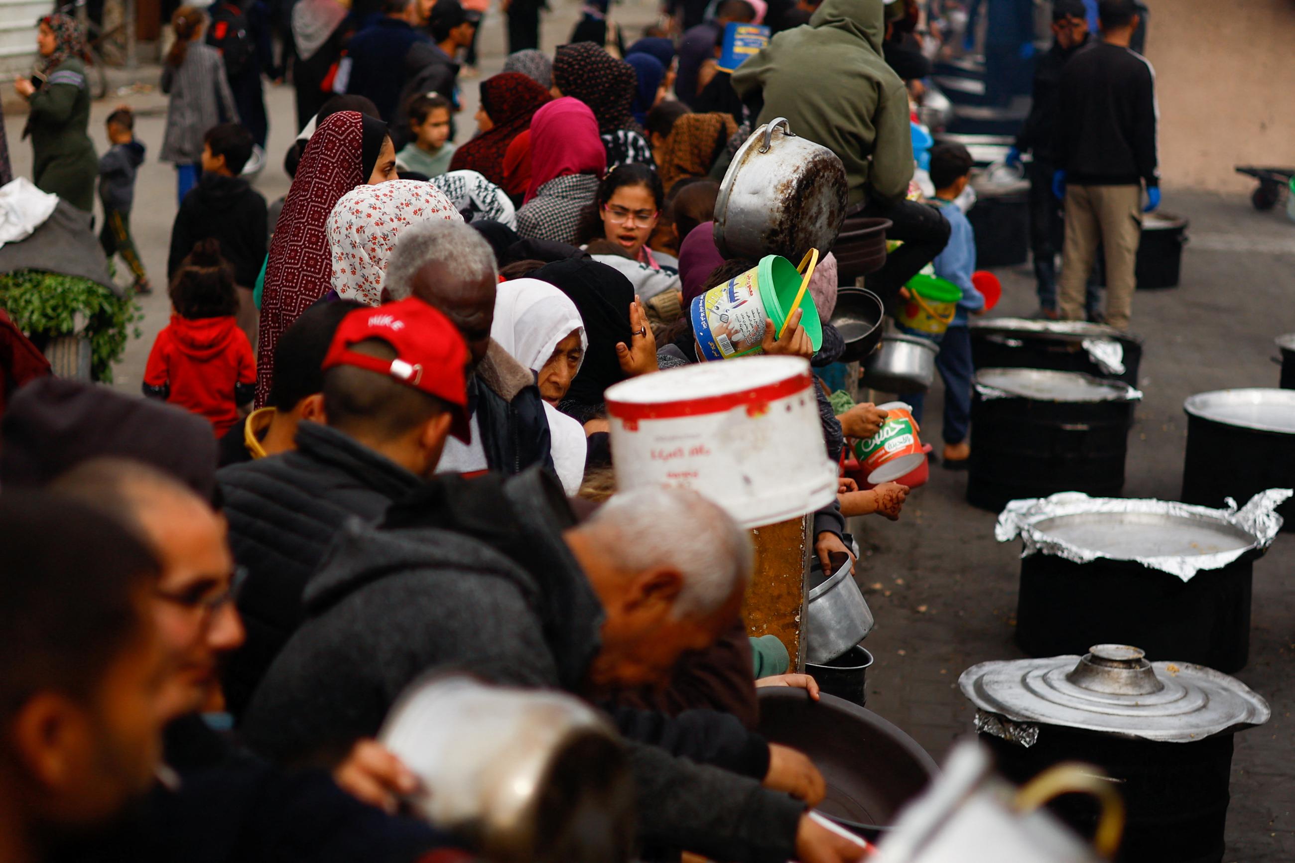 Palestinians wait to receive food cooked by a charity kitchen amid shortages of food supplies.