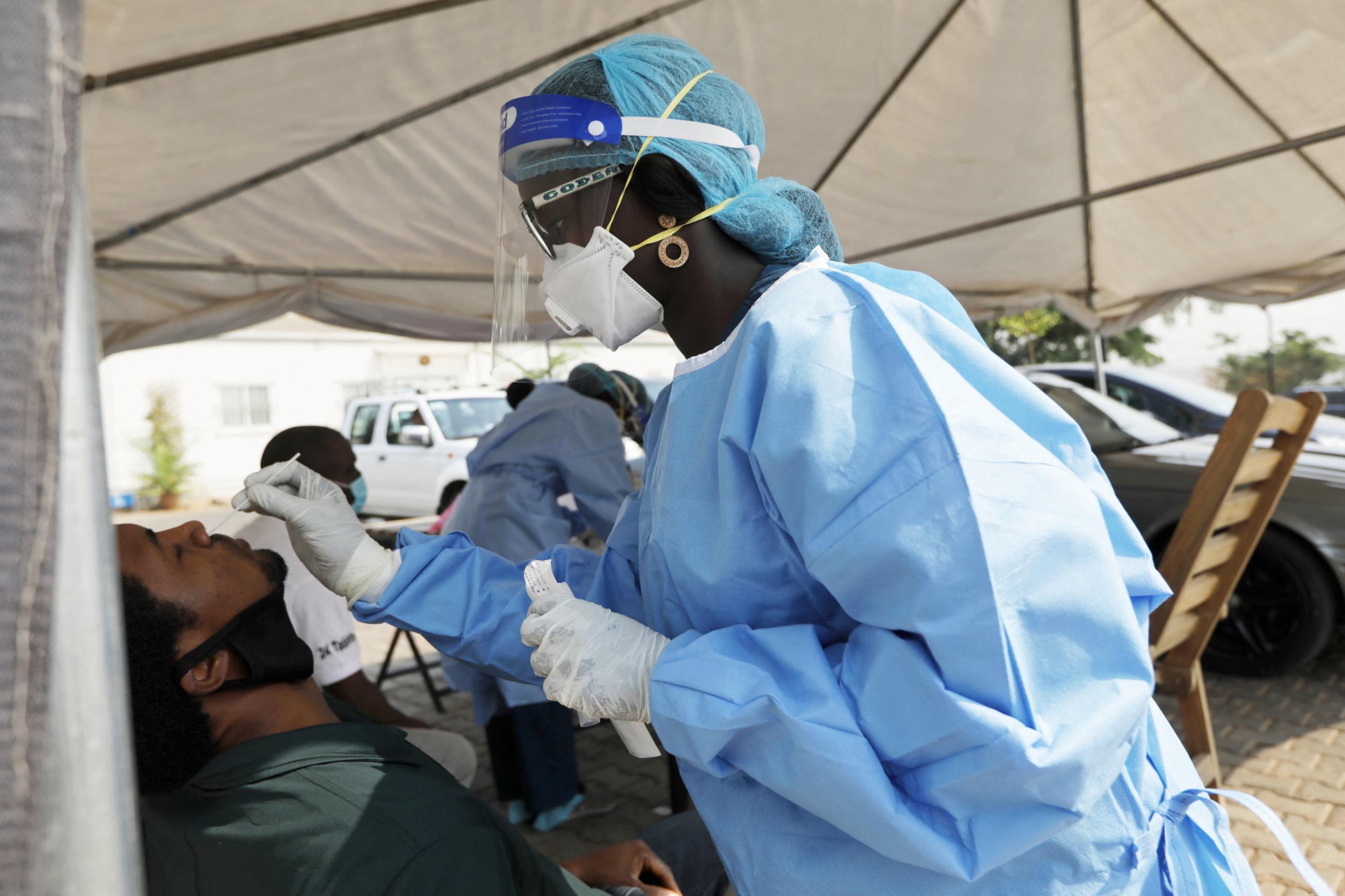 A health worker collects a nose swab from a man at a drive-through sample collection center for COVID-19.