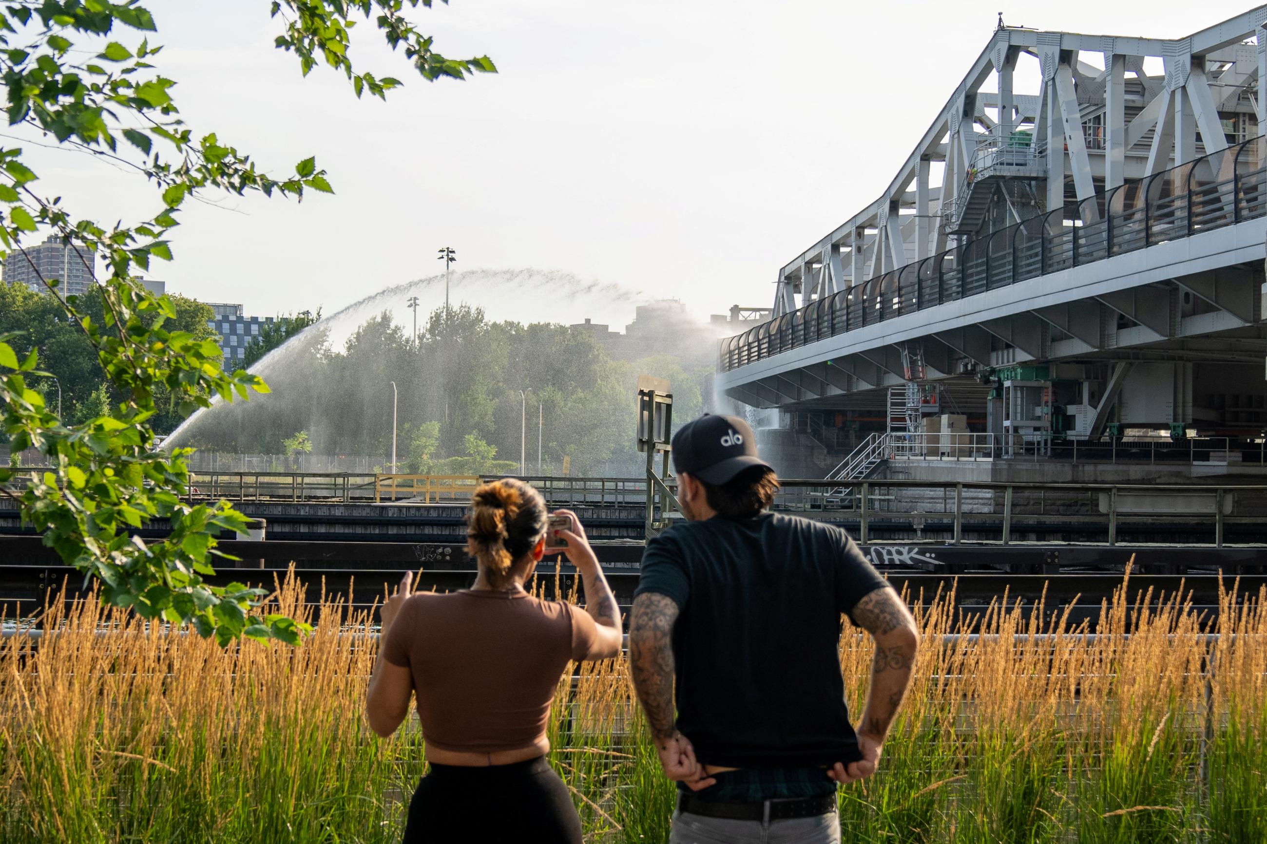 People watch the Fire Department of New York (FDNY) and bridge maintenance workers attempt to cool off the 3rd avenue Bridge after it was stuck in the boat passage position after experiencing overheating.