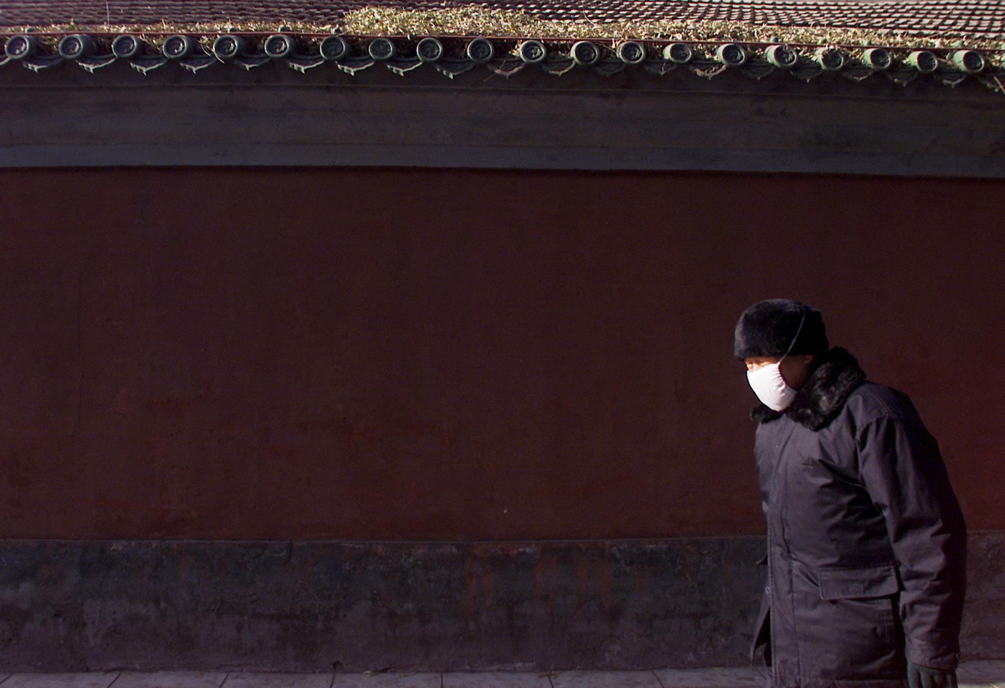 An elderly Chinese man, bundled up for freezing temperatures, walks past an old building, in Beijing, China, on December 9, 2002.