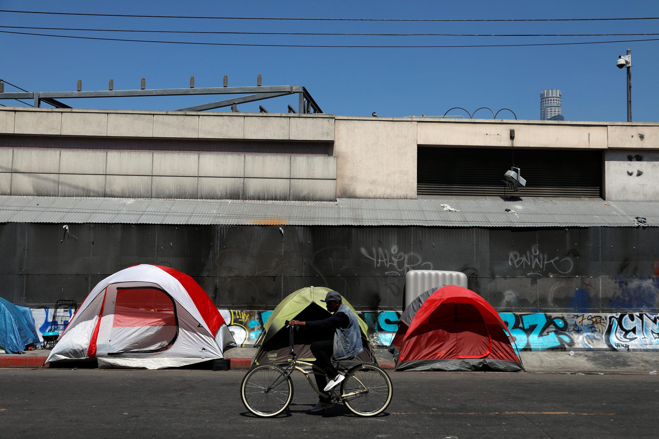 A cyclist passes by tents and tarps erected by homeless people along sidewalks in the skid row area of downtown Los Angeles, California, on June 28, 2019.