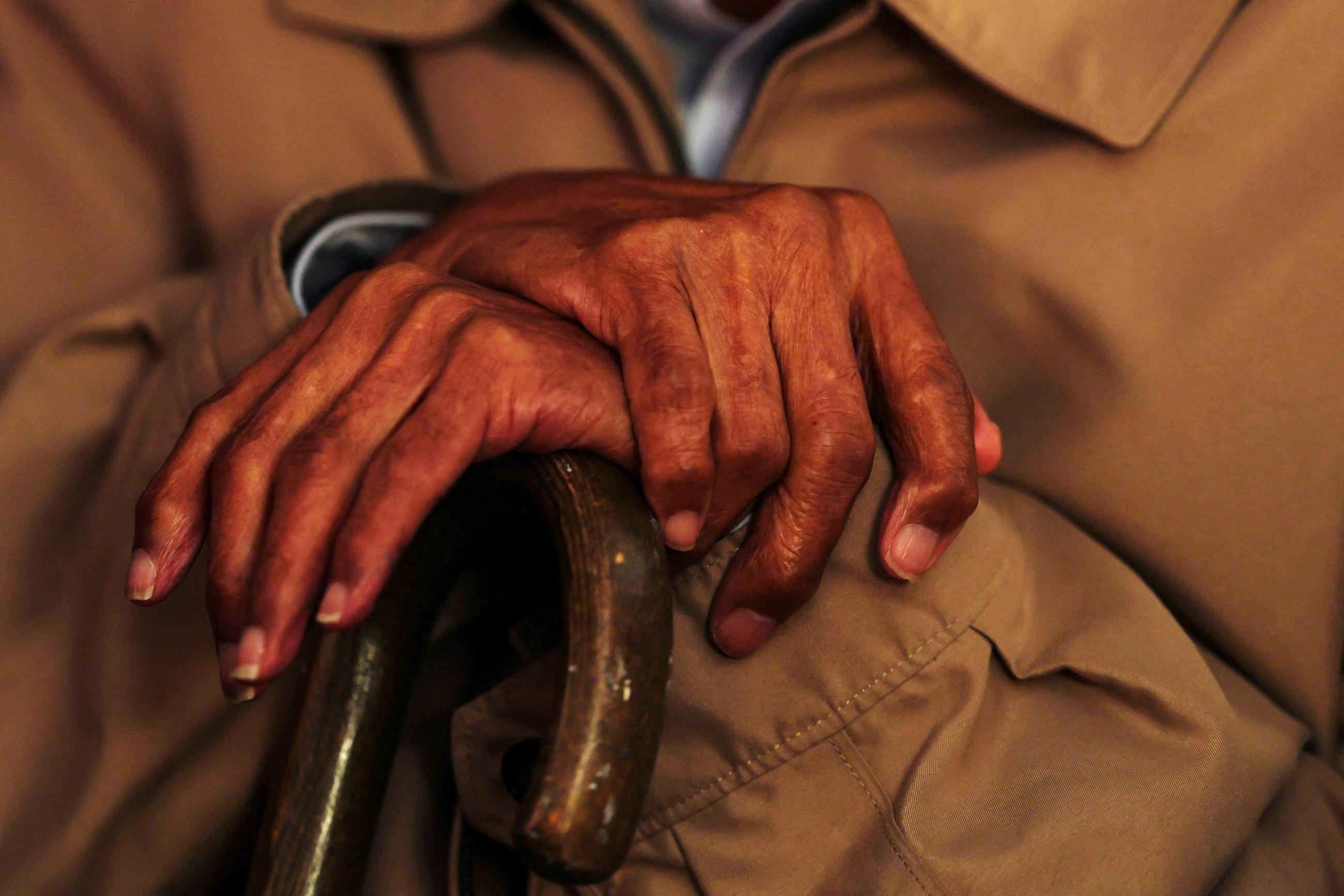 An elderly man crosses his hands on a cane during a funeral in the Bronx borough of New York City, U.S., June 12, 2024.