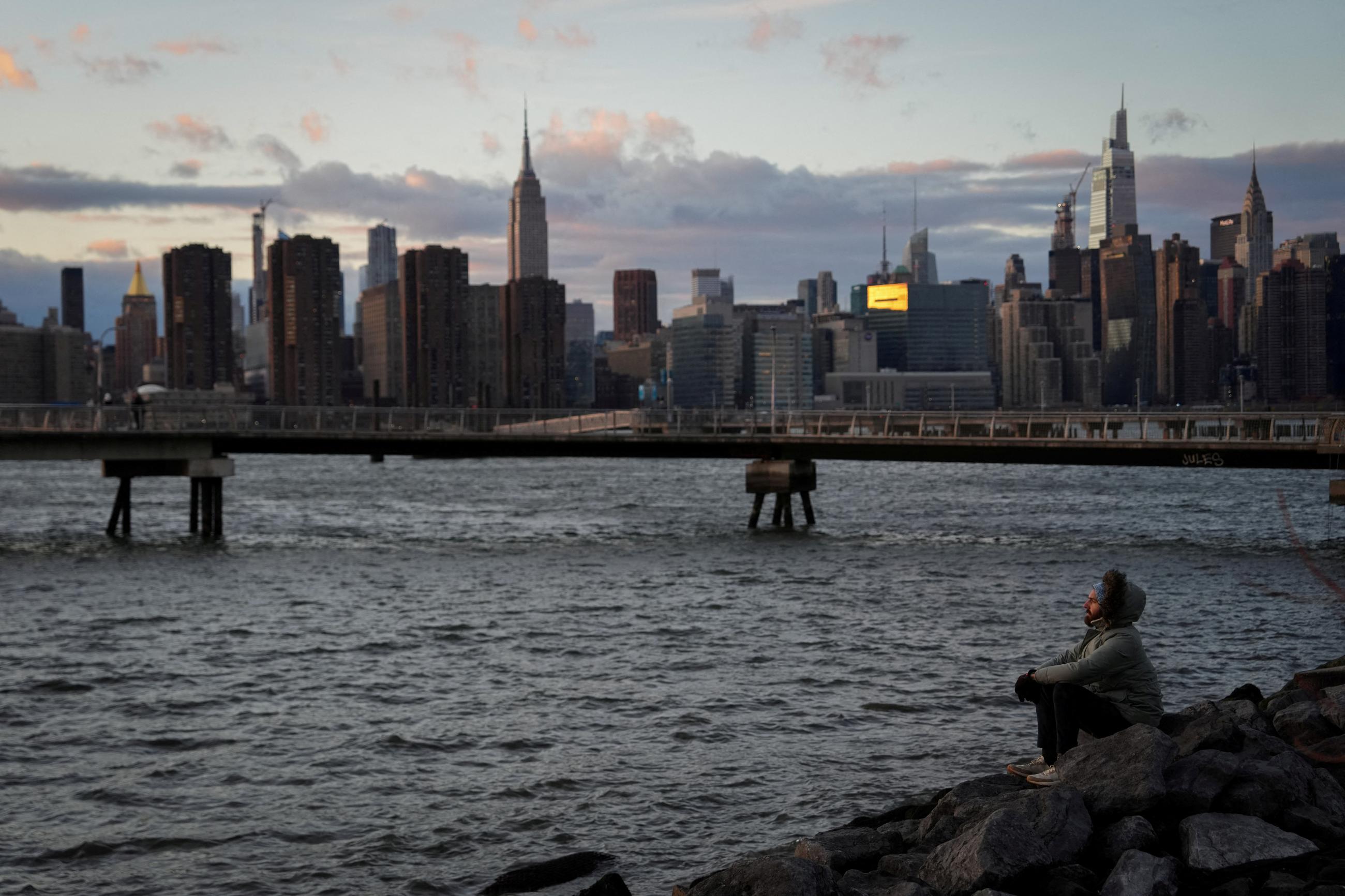 A person watches the sunset as they sit by the East River, in Brooklyn, New York City, on January 2, 2025.