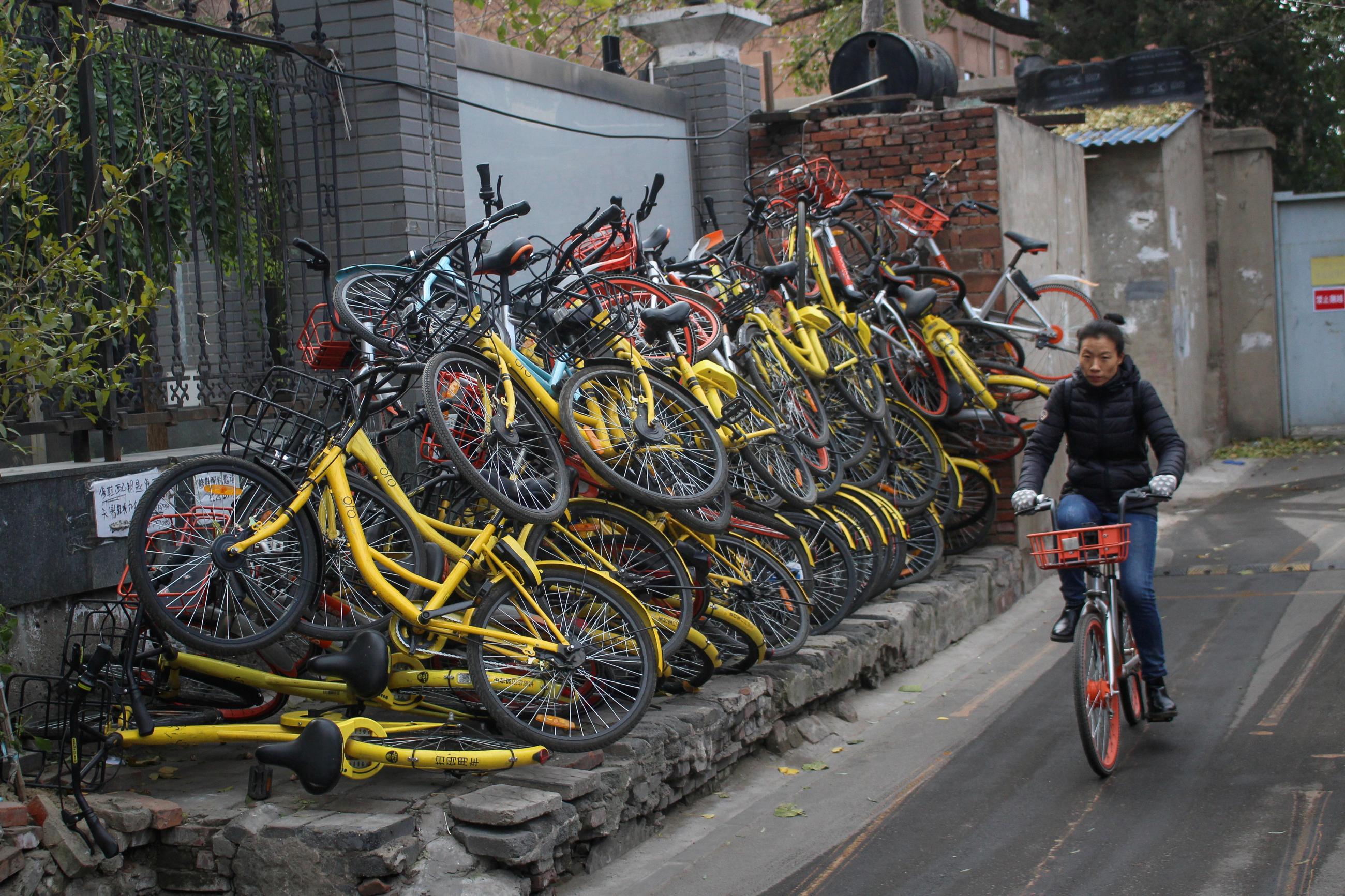 A woman rides a bicycle past shared bikes at a hutong, in Beijing, Chin