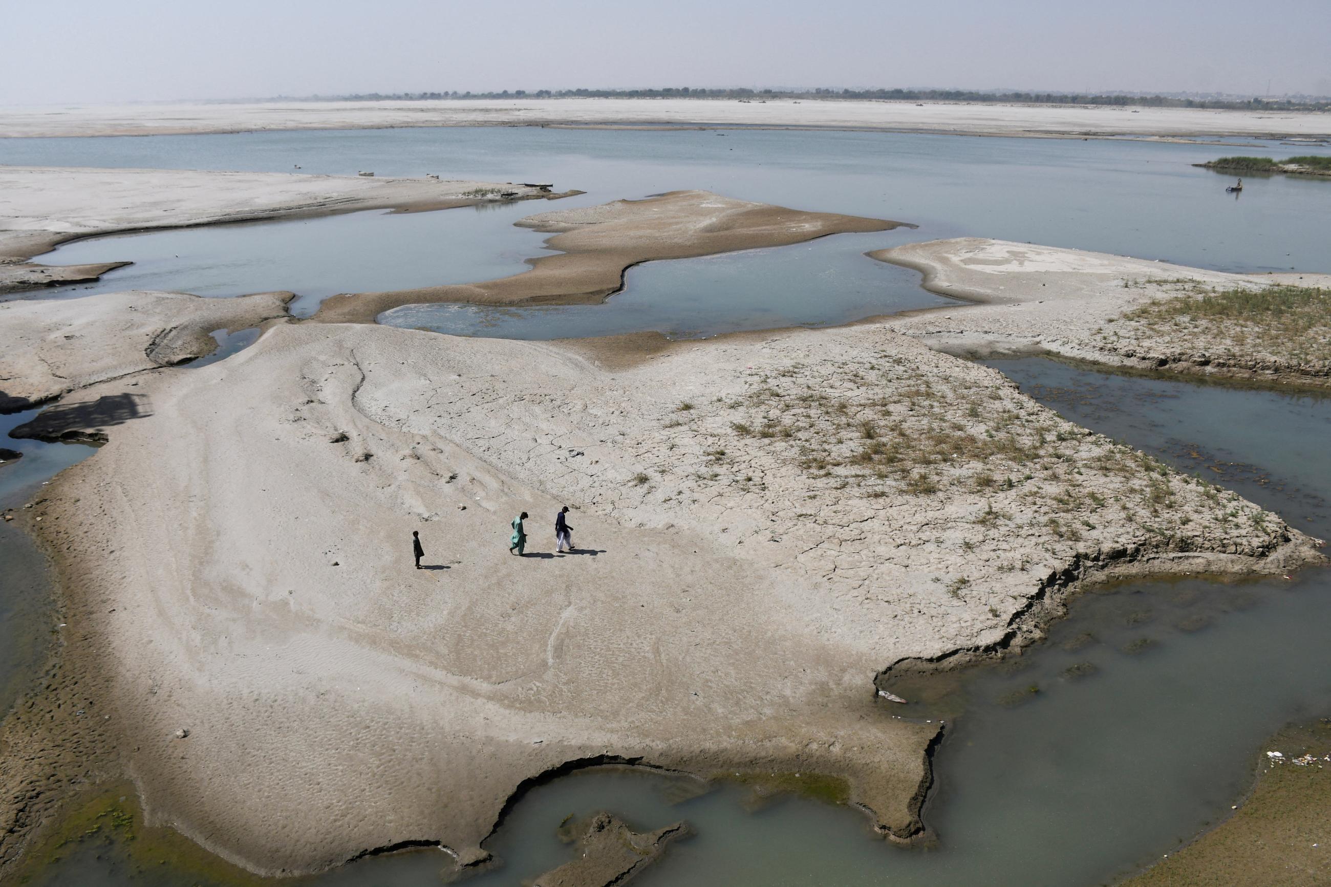 People walk on the dry patch of the Indus River, in Jamshoro, Pakistan, on March 15, 2025. 