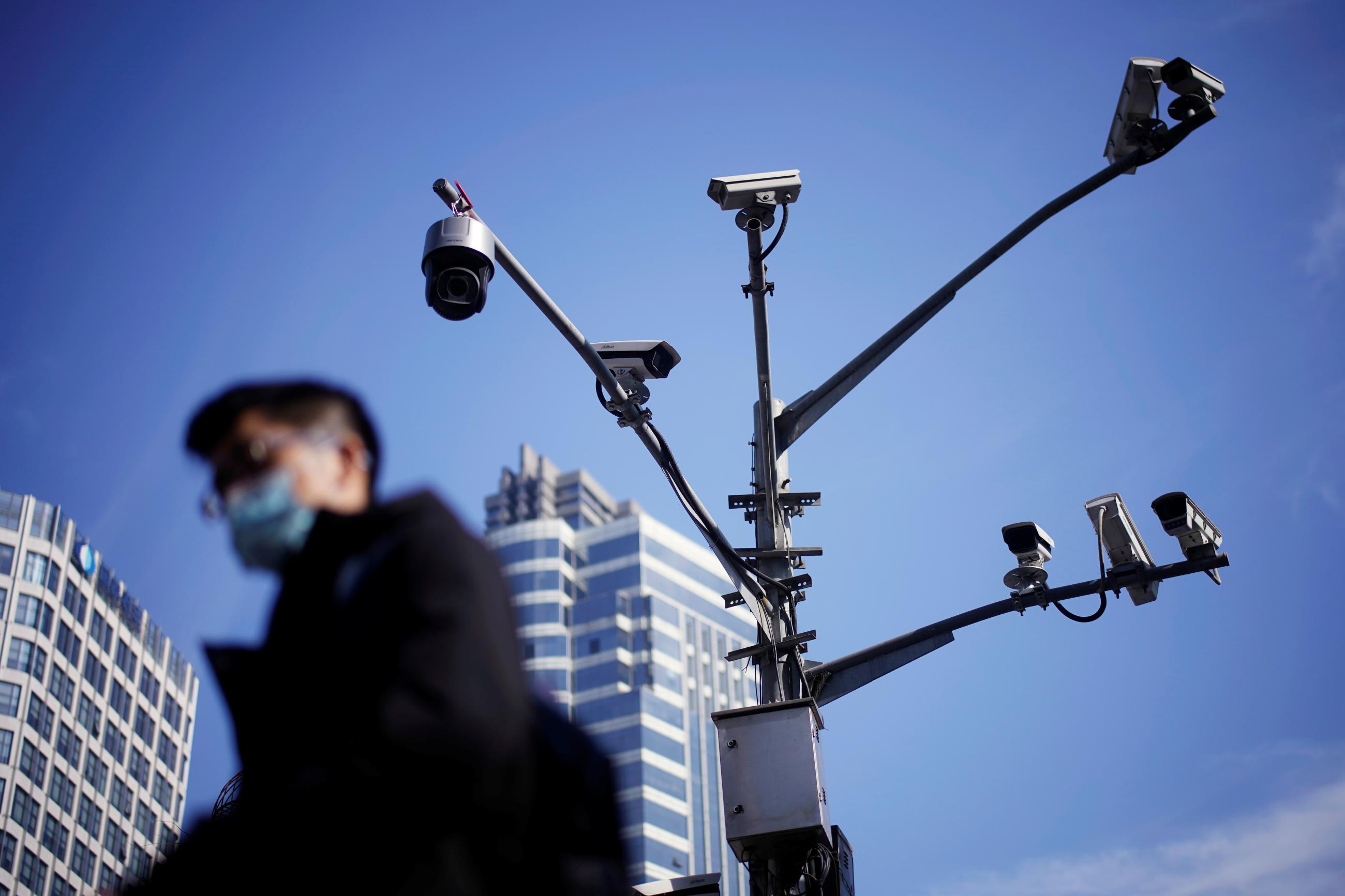 A man wearing a face mask walks past surveillance cameras following the COVID-19 outbreak, in Shanghai, China, on January 14, 2021. 