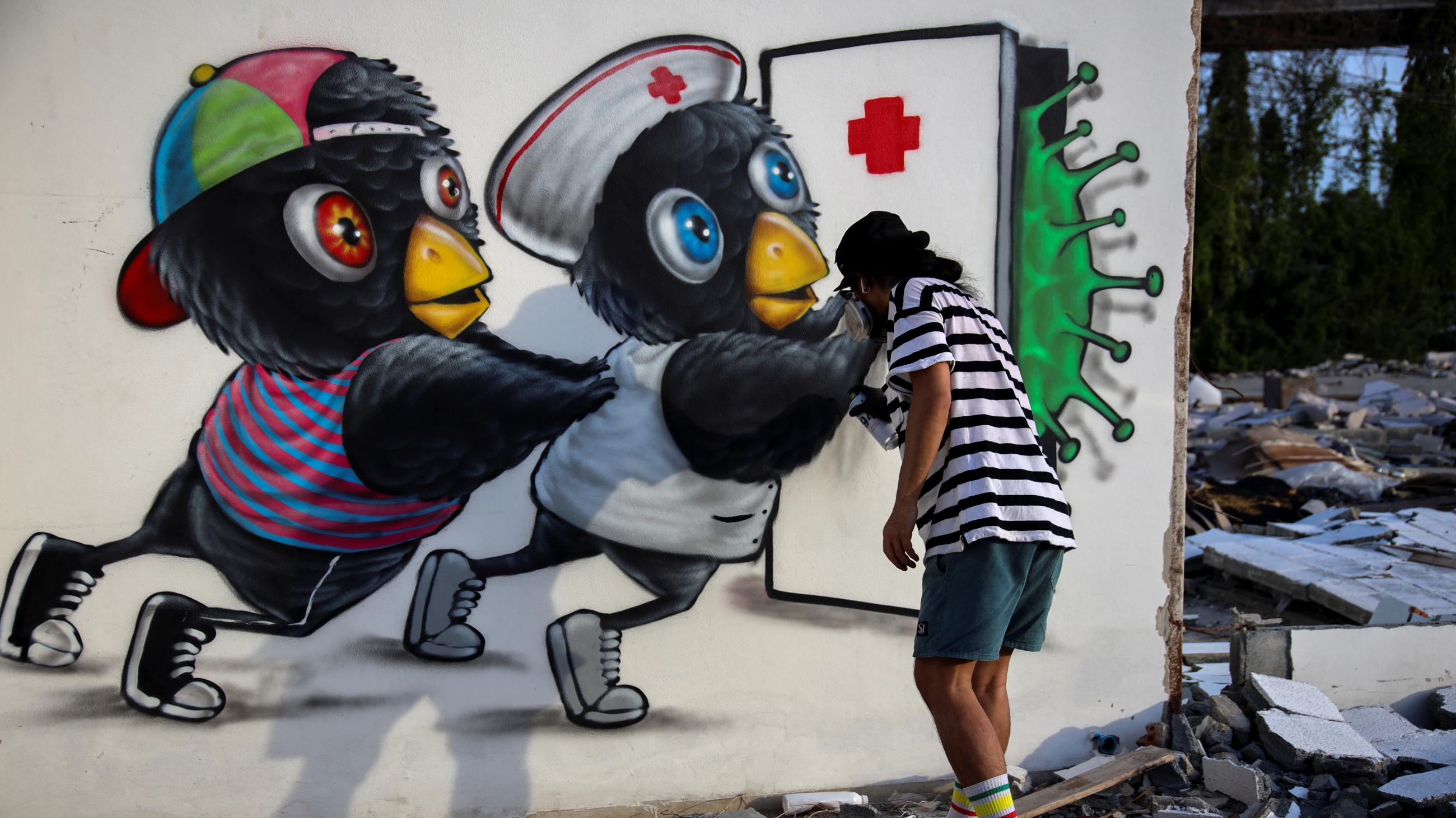 Thai street artist Mue Bon paints a scenario depicting characters attempting to keep a COVID virus at bay, in Bangkok, Thailand, on May 21, 2020. 