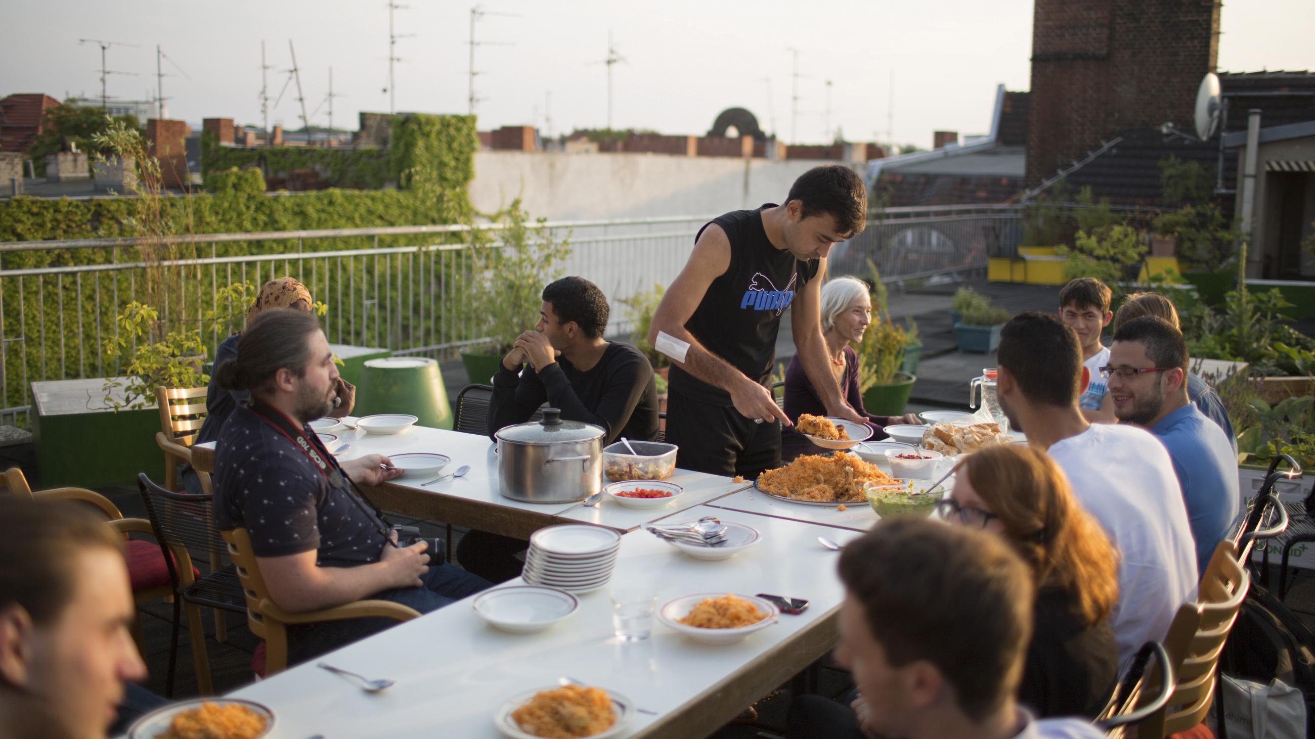 People seeking refuge in a new country live alongside German residents in the "Sharehaus Refugio" community in Berlin, Germany (2015). Neighbors in the five-story, century-old building meet for meals on the rooftop garden.