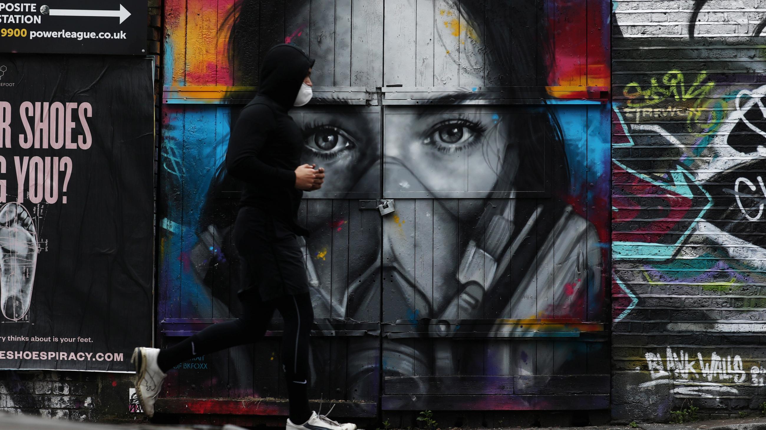 A man wearing a face mask jogs by street art in Brick Lane, in London, on April 18, 2020.