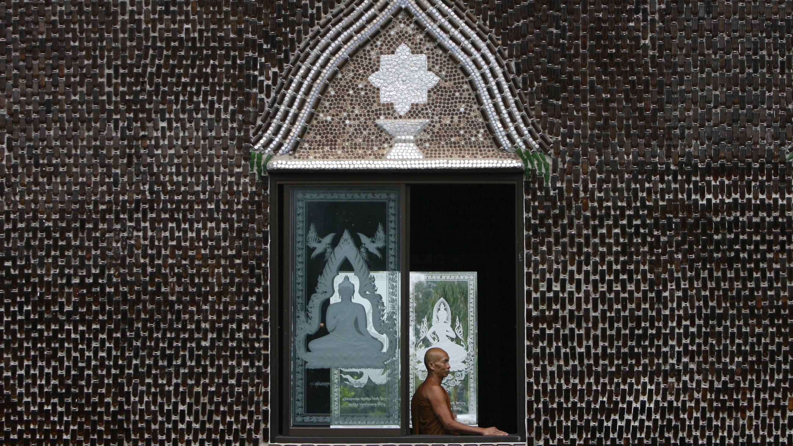 A Buddhist monk looks out of the window of the Wat Pa Maha Chedi Kaew temple, built with more than a million glass bottles