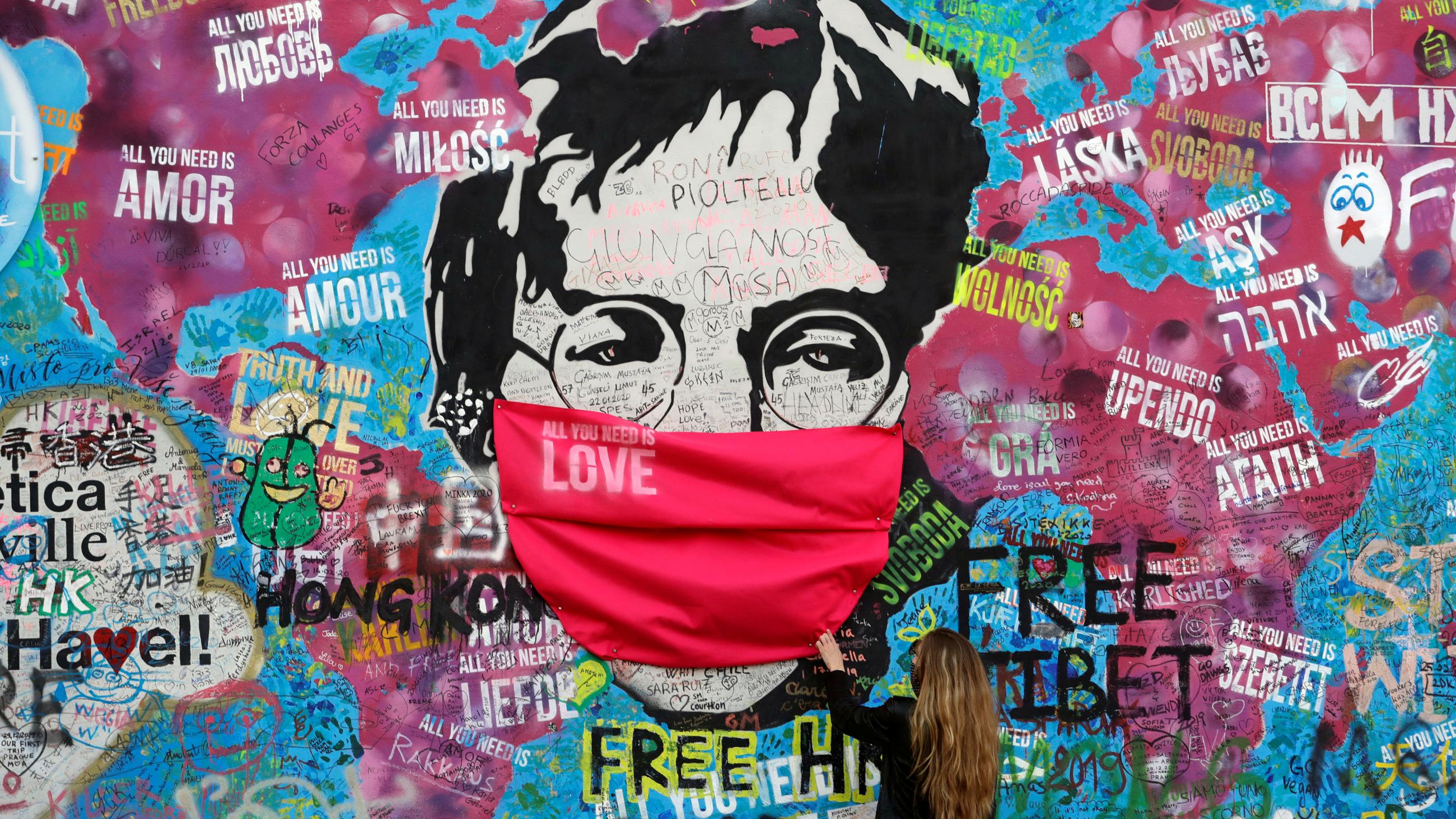 A woman wearing a face mask during the COVID-19 pandemic touches the legendary graffiti-covered John Lennon Wall in Prague, Czech Republic, on April 6, 2020.