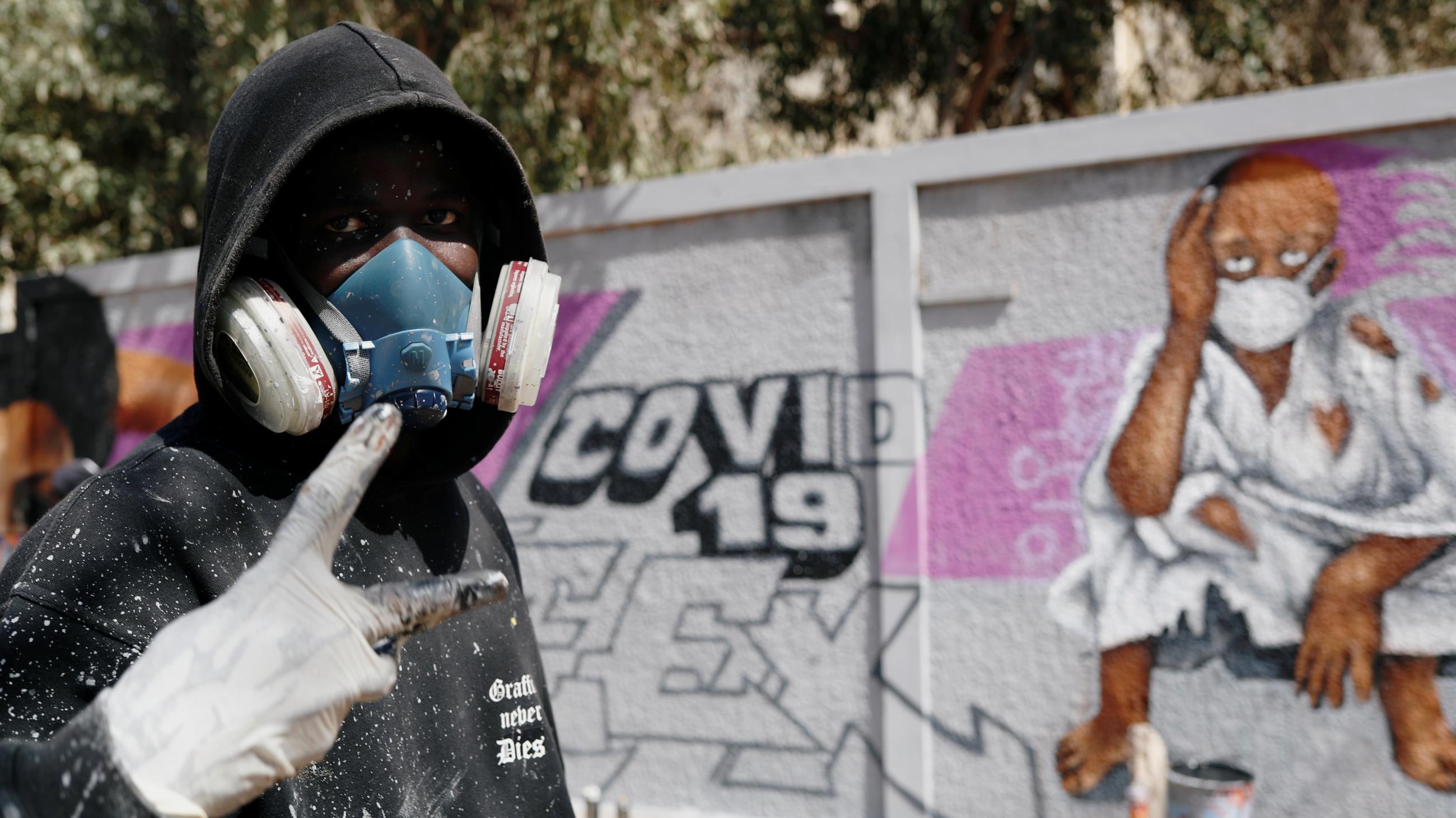 Serigne Boye aka Zeus, a street artist from RBS crew, flashes a peace sign as he stands beside his mural meant to encourage people to protect themselves during the coronavirus outbreak in Dakar, Senegal, on March 25, 2020.