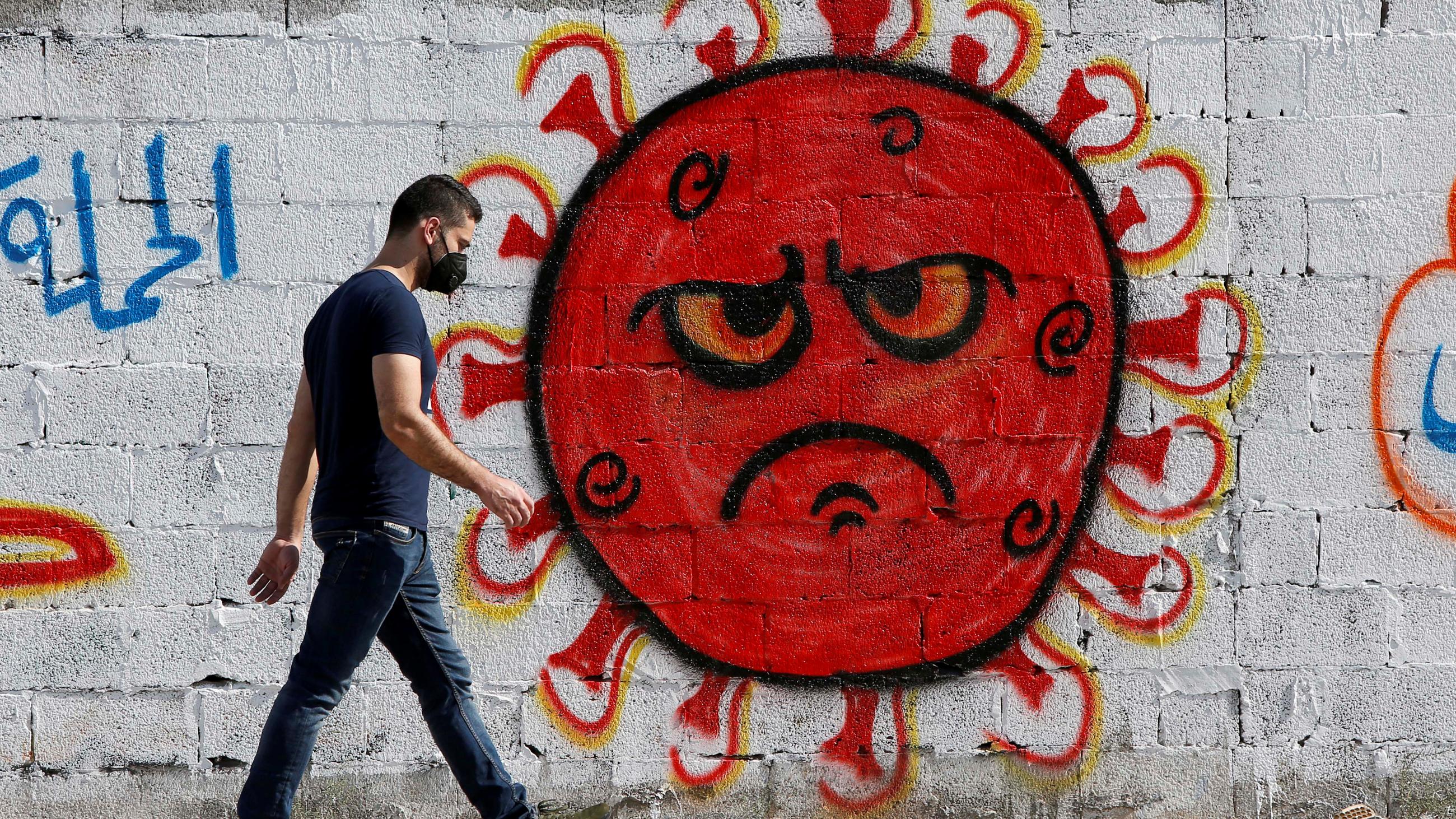 A Palestinian man walks past cartoon-style street art of the novel coronavirus SARS-CoV-2, with its signature spike proteins, in Gaza City, on October 4, 2020.