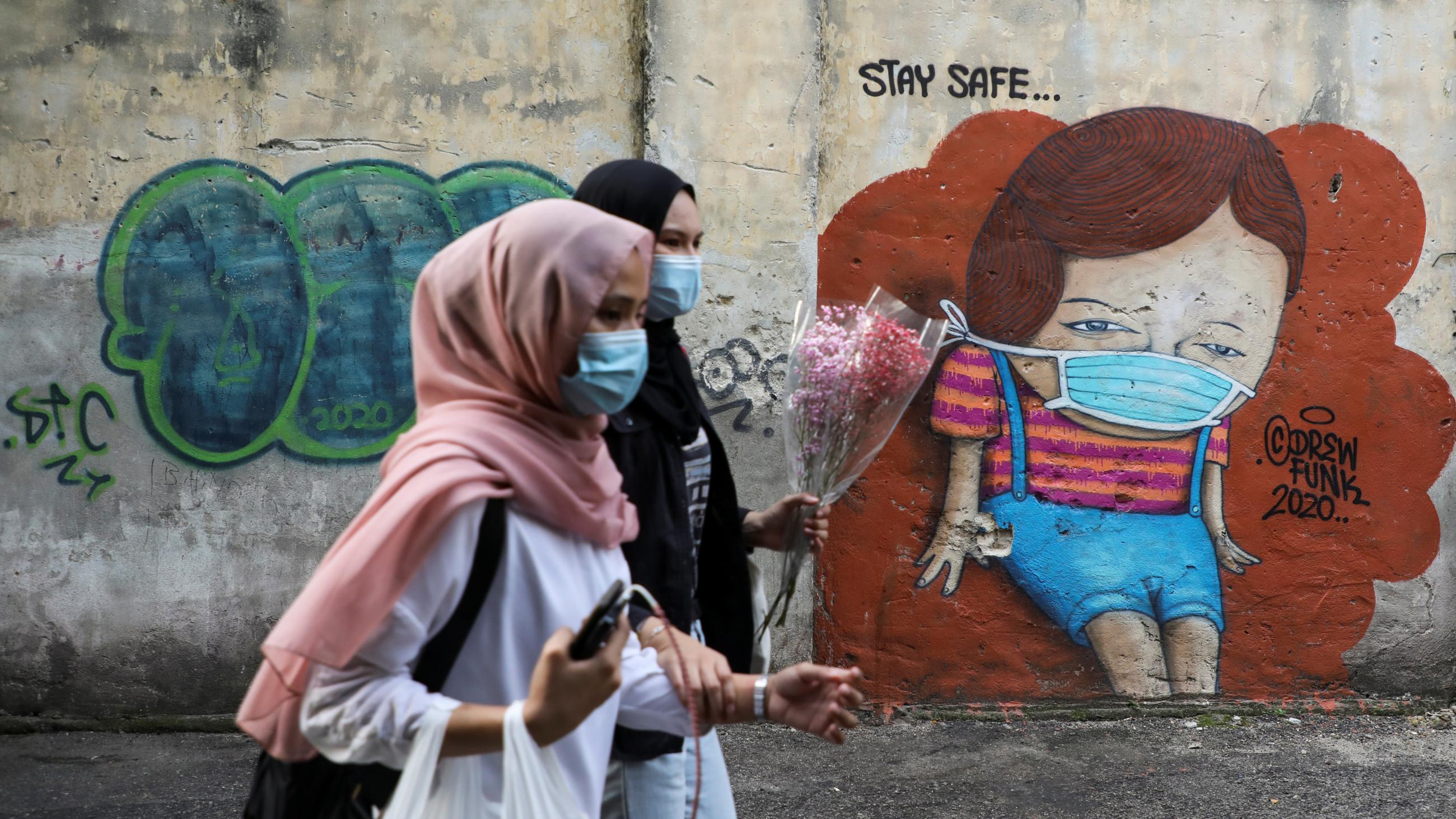 Women wearing protective masks walk past street art encouraging people to "stay safe" amid the coronavirus pandemic in Kuala Lumpur, Malaysia, on September 18, 2020.