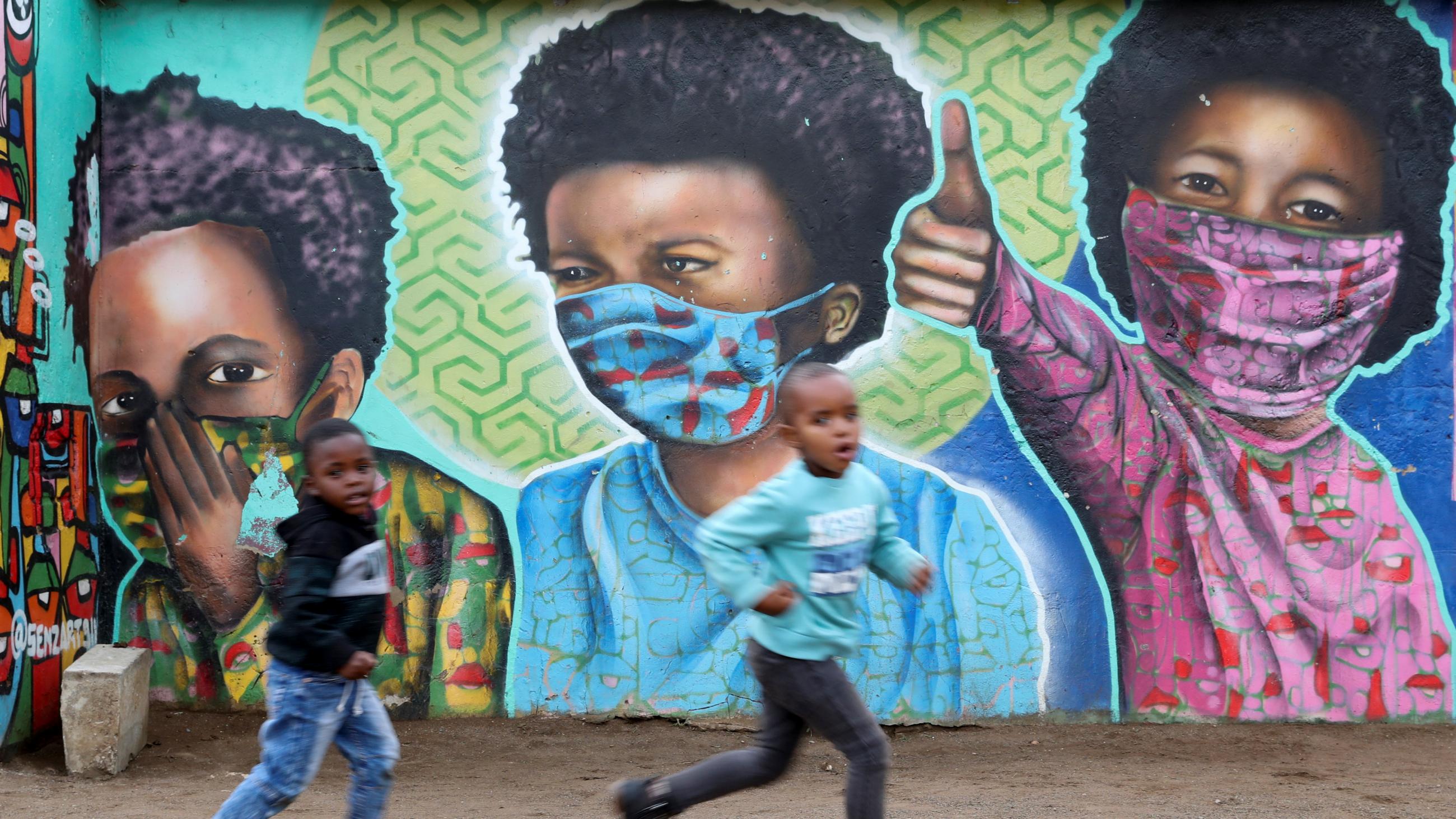 Boys run past a mural by graffiti artist Senzart911 during the COVID outbreak, in Kliptown, the oldest residential district of Soweto, South Africa, on October 27, 2021.