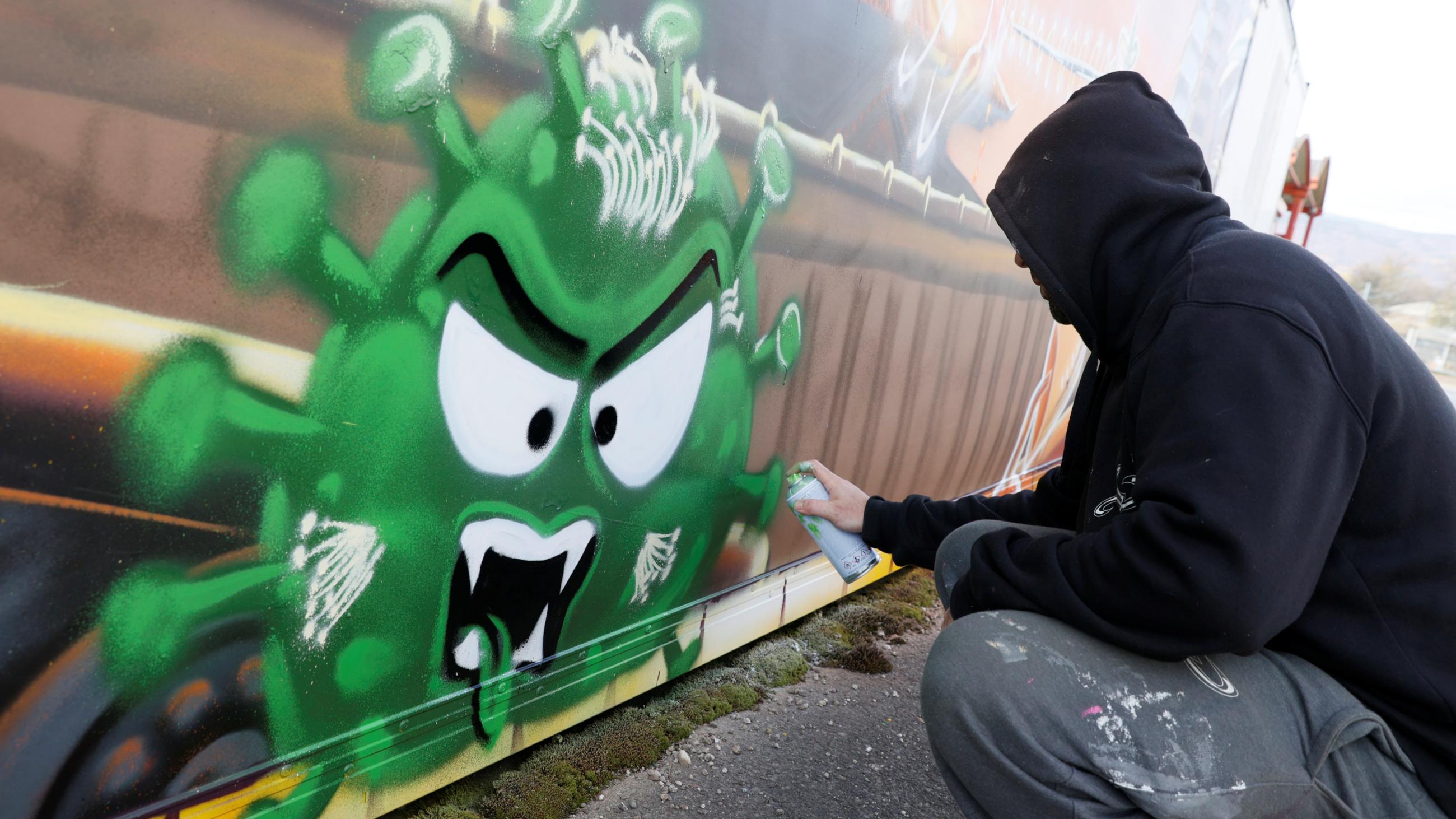 Artist David "S.I.D." Perez spray paints an image representing two vaccines fighting against a virus, in Gland, Switzerland, on December 3, 2020.