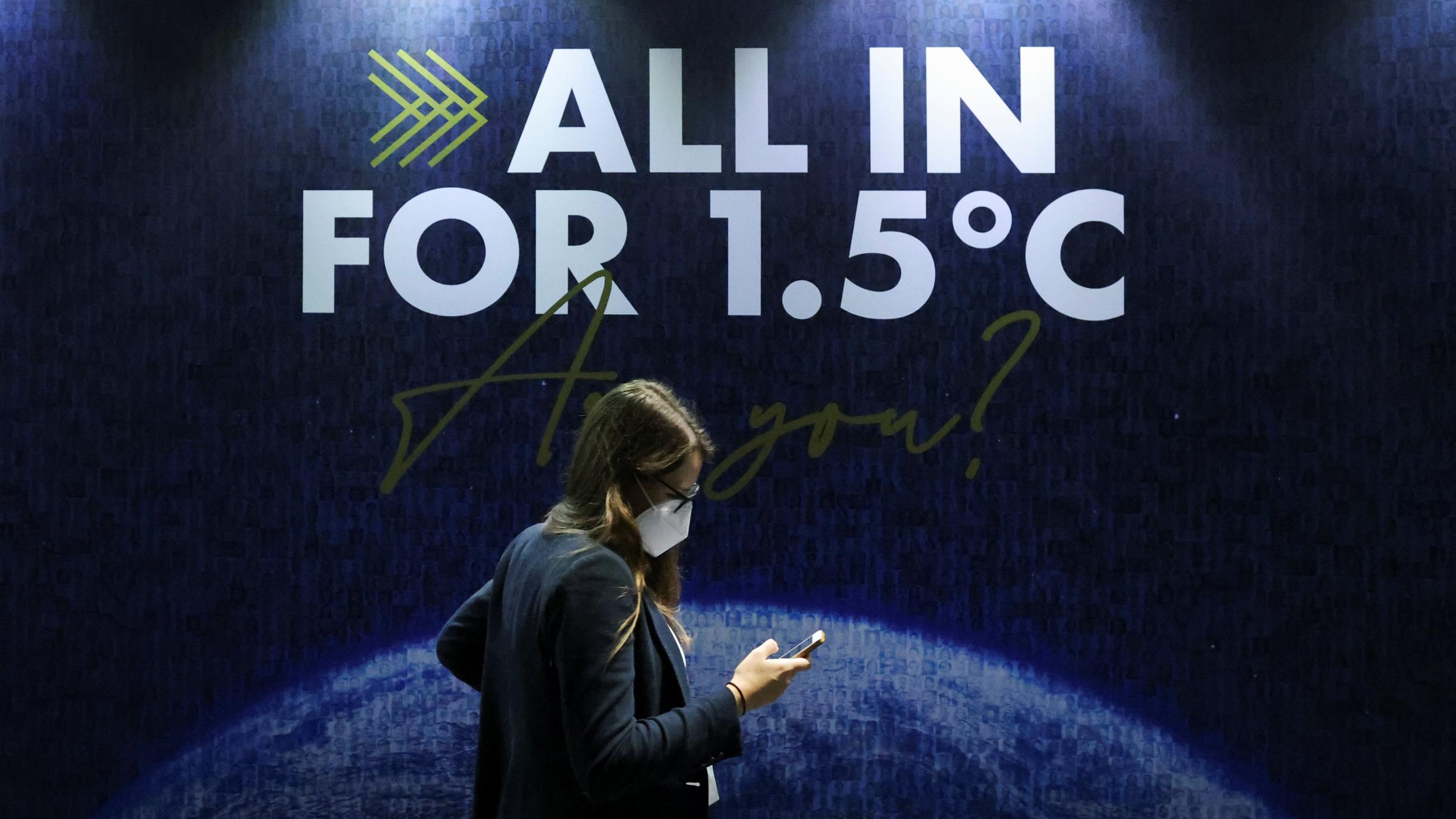 A delegate walks past an "all in for 1.5" sign during the climate conference. The phrase refers to the 2015 Paris Agreement goal to limit global warming to 1.5 degrees Celsius.