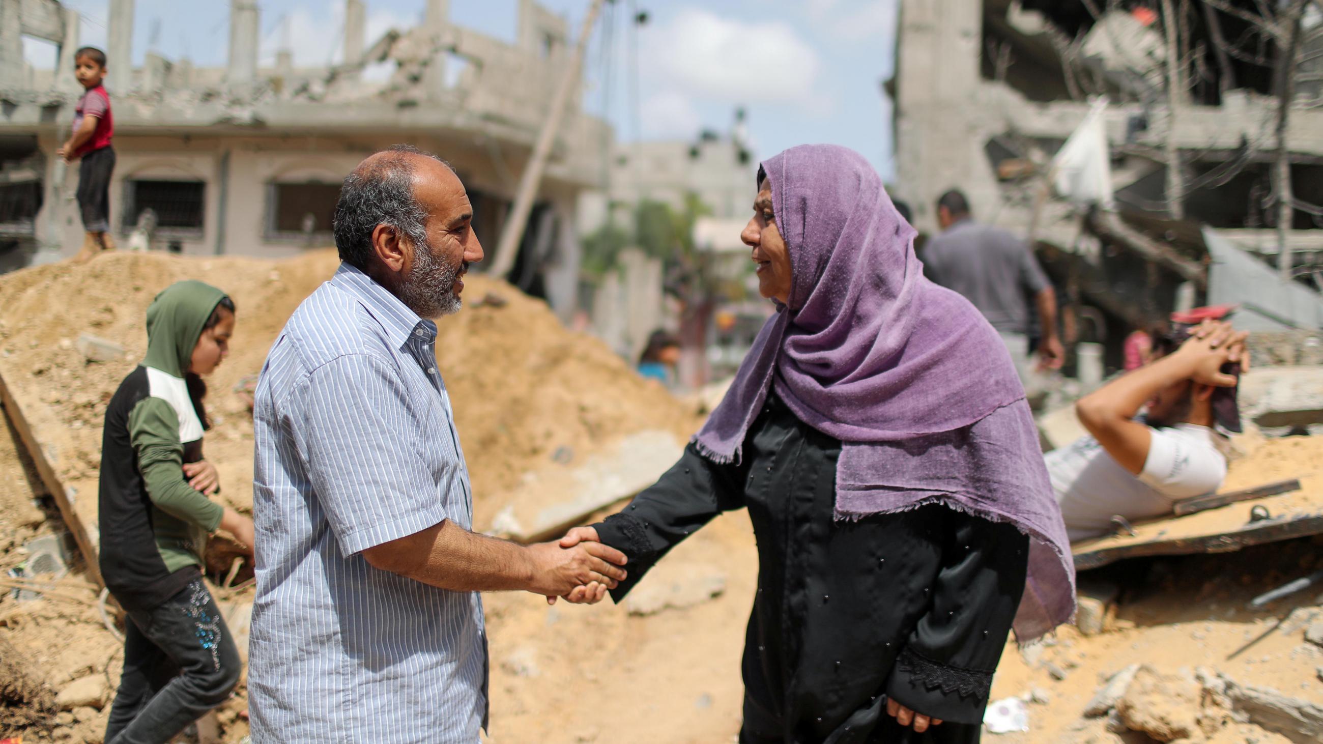 A Palestinian man and a Palestinian woman from shake hands after returning to their destroyed houses following an Israel-Hamas truce, in Beit Hanoun in the northern Gaza Strip on May 21, 2021. REUTERS/Mohammed Salem