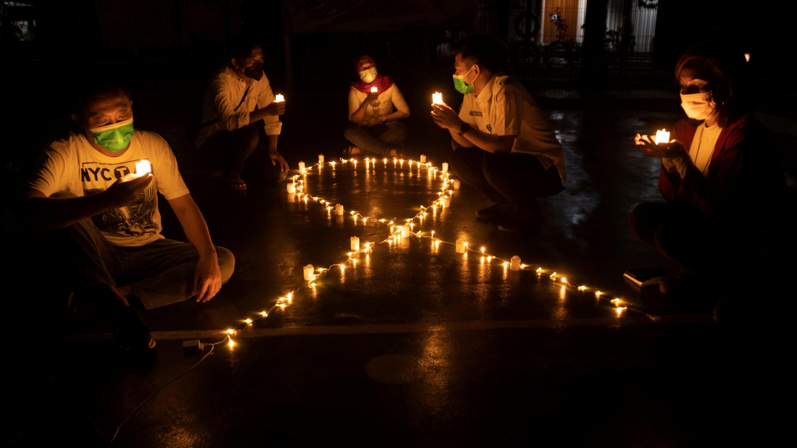 Activists sit next to candles laid out in the shape of an AIDS ribbon, commemorating World Aids Day in Jakarta, Indonesia, on December 1, 2021. 