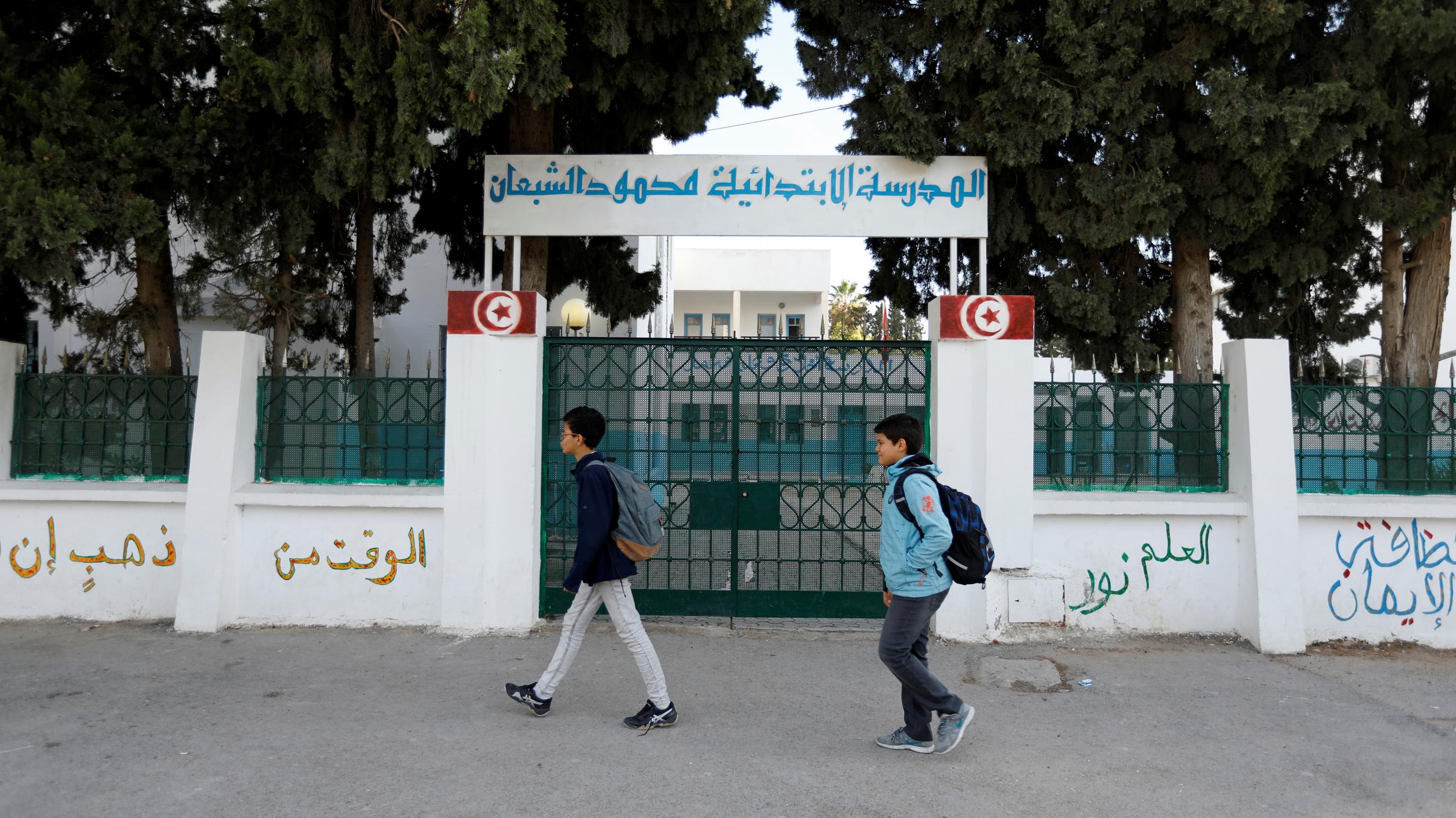 Children walk past the closed gates of a school in Tunisia
