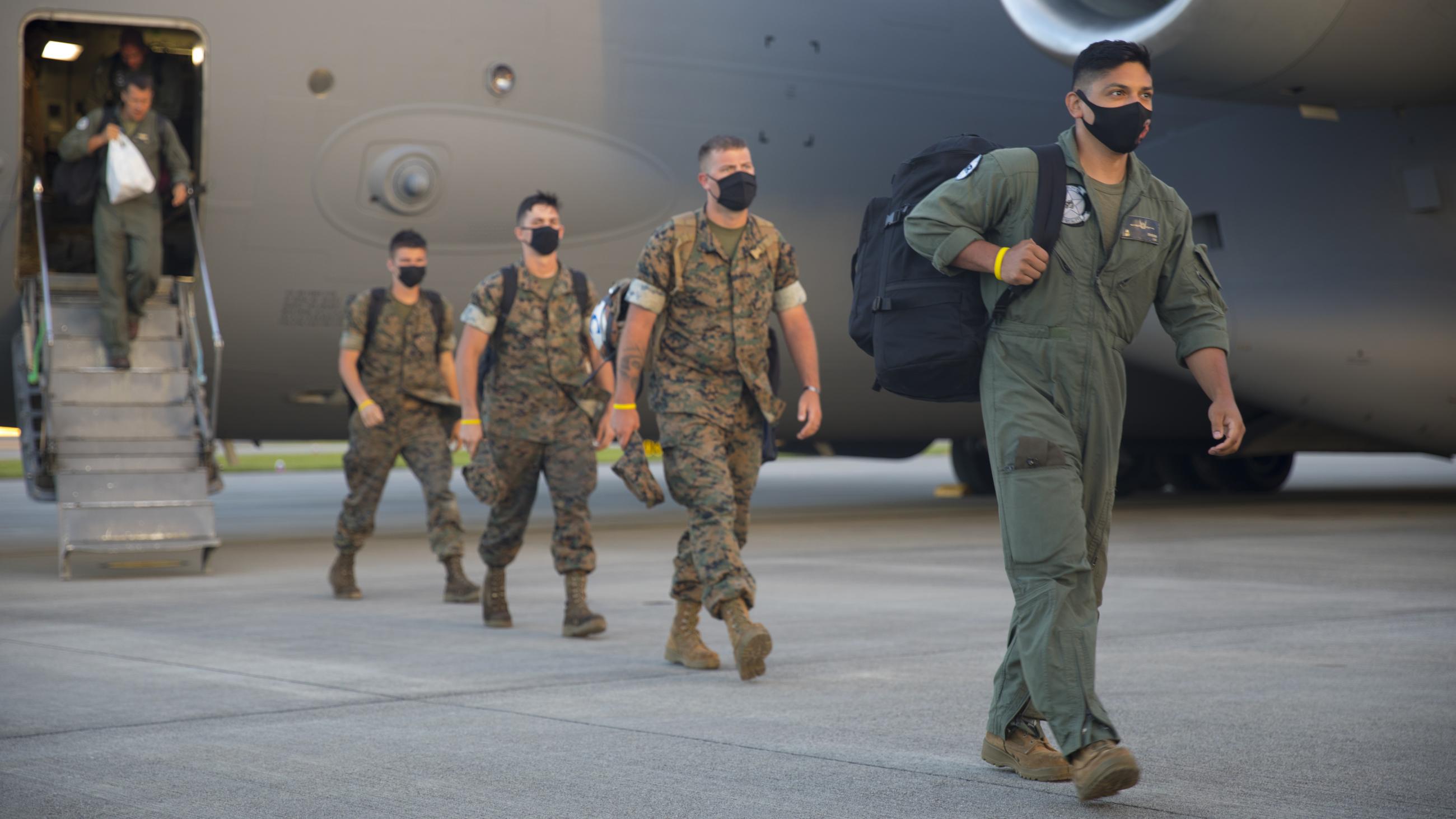 Four uniformed U.S. Marines file out of a grey personnel carrier aircraft.