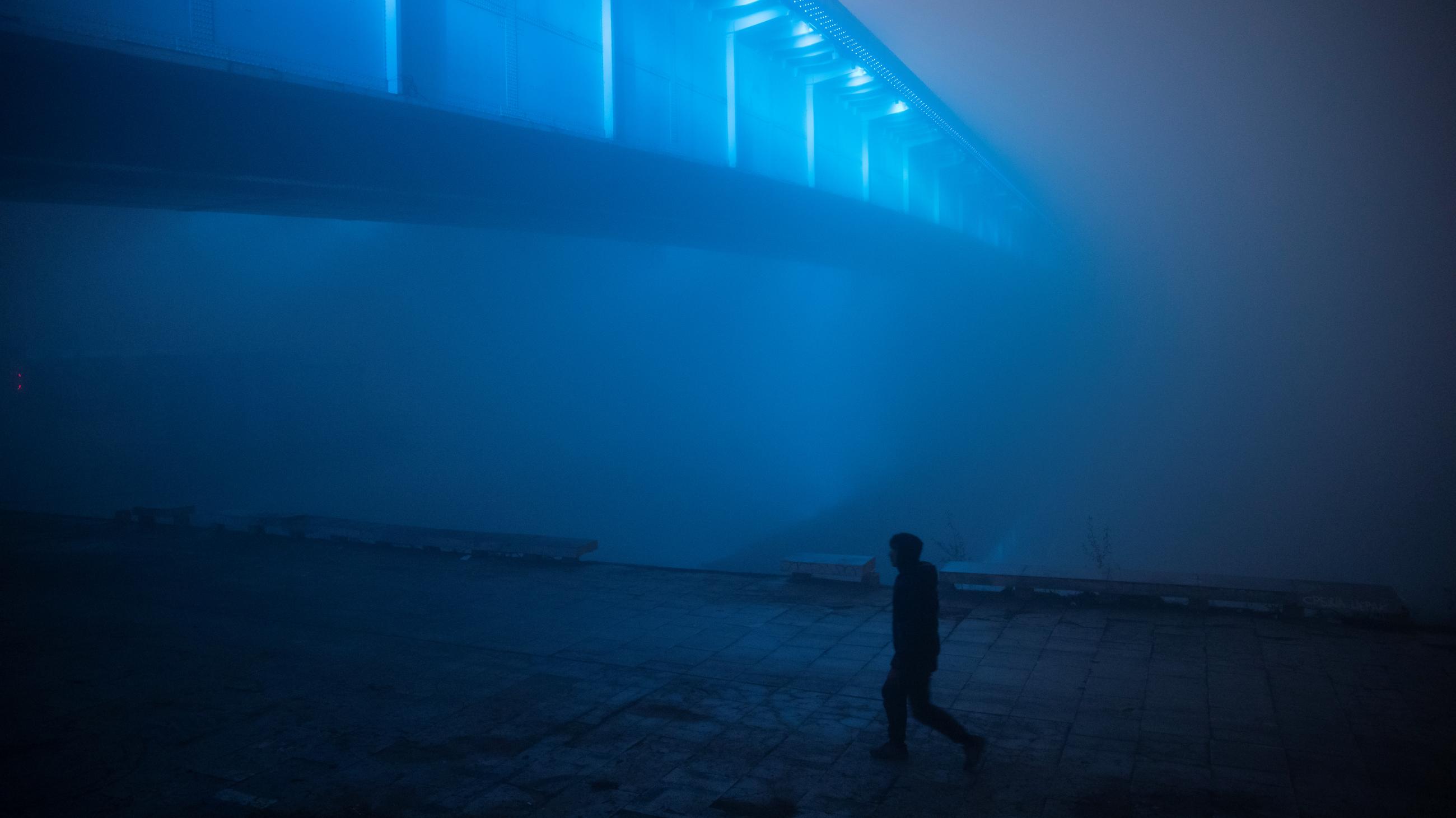 A man, illuminated by blue lights, walks under the Brankov bridge amidst dense fog and smog in Belgrade, Serbia, on January 15, 2020.