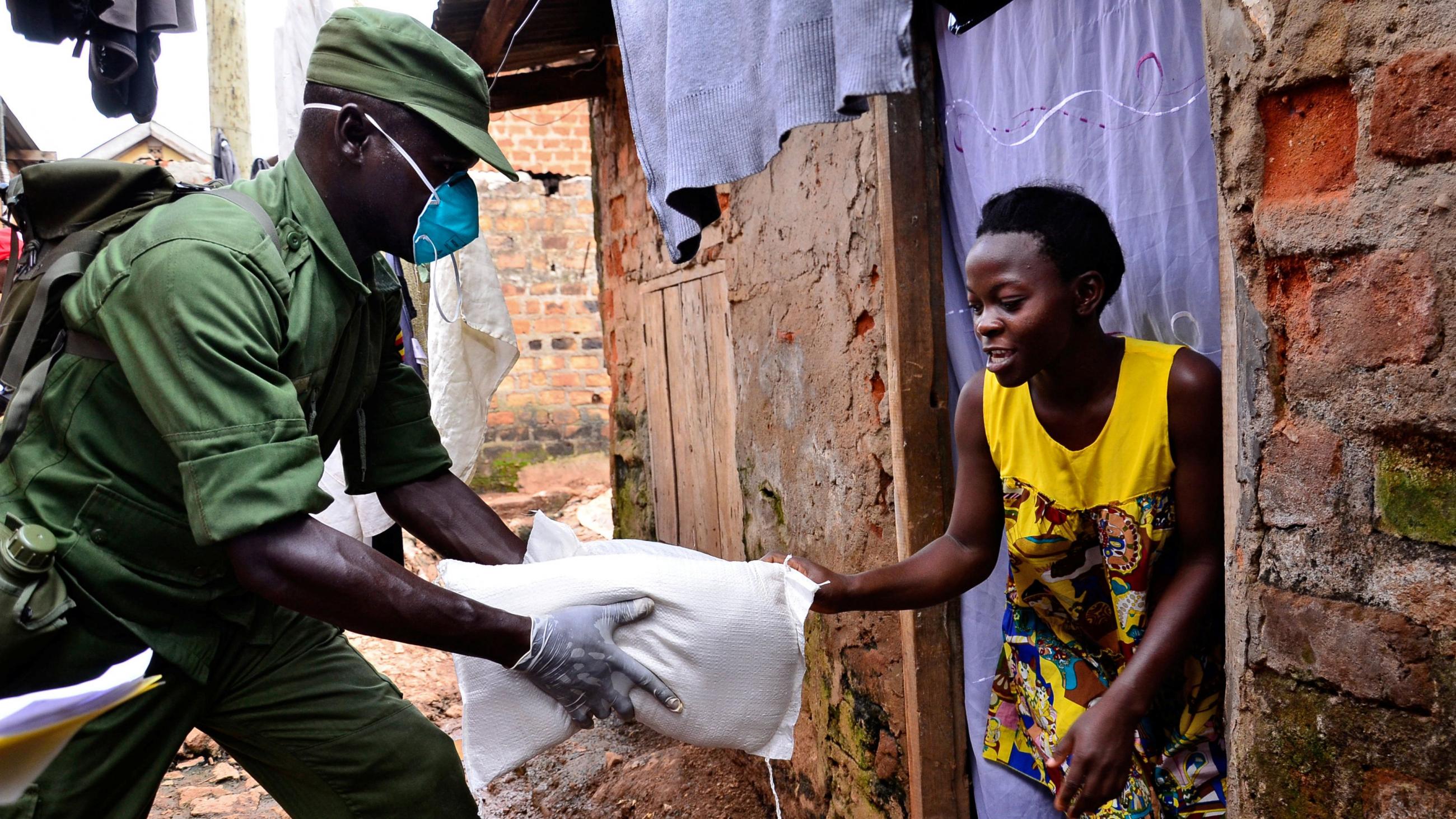 A Ugandan soldier in a green uniform gives a bag a food to a young woman in a yellow dress.