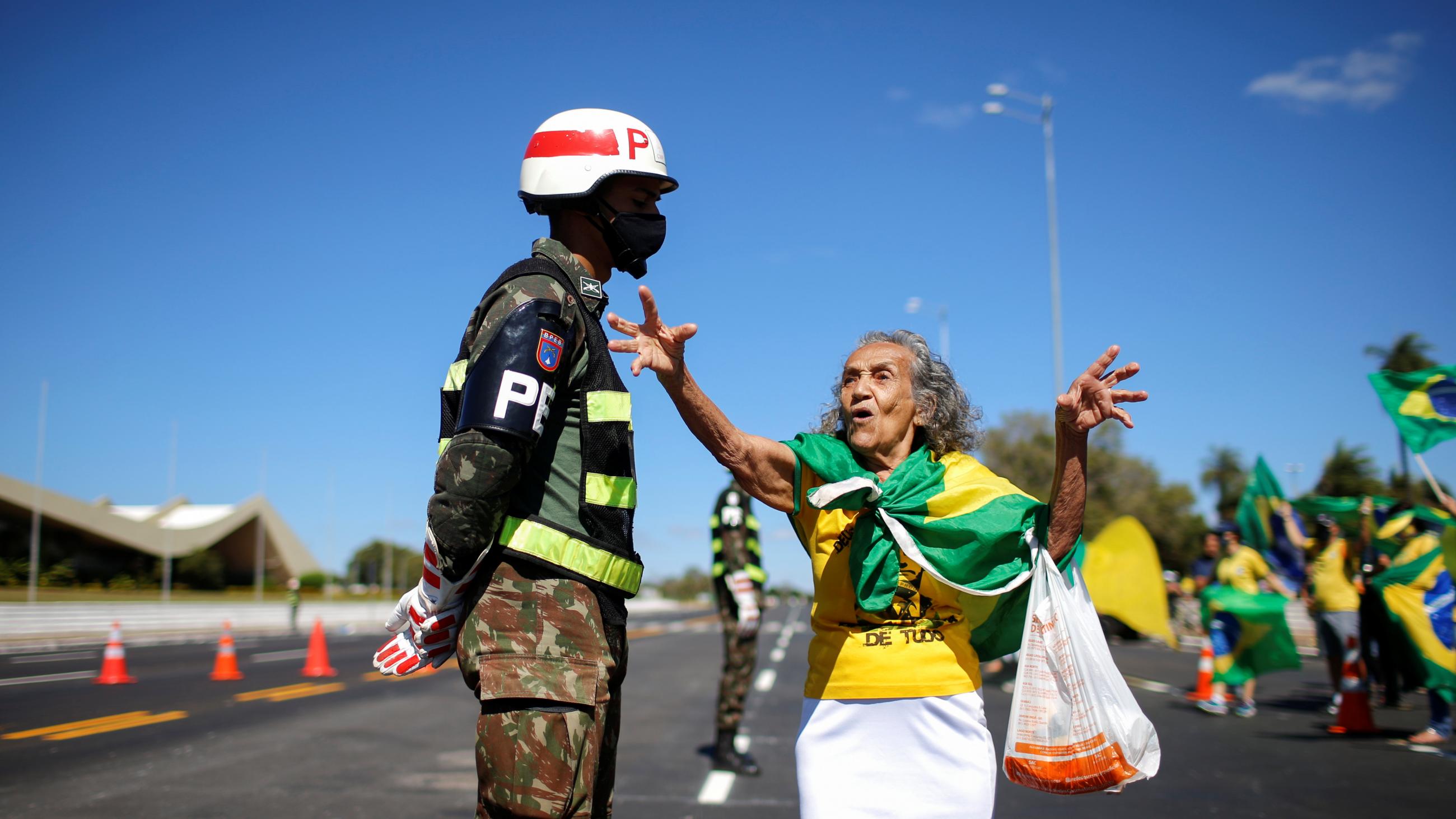 An old woman wrapped in Brazil's green and yellow flag confronts a Brazilian soldier in front of Brazil's Army Headquarters.