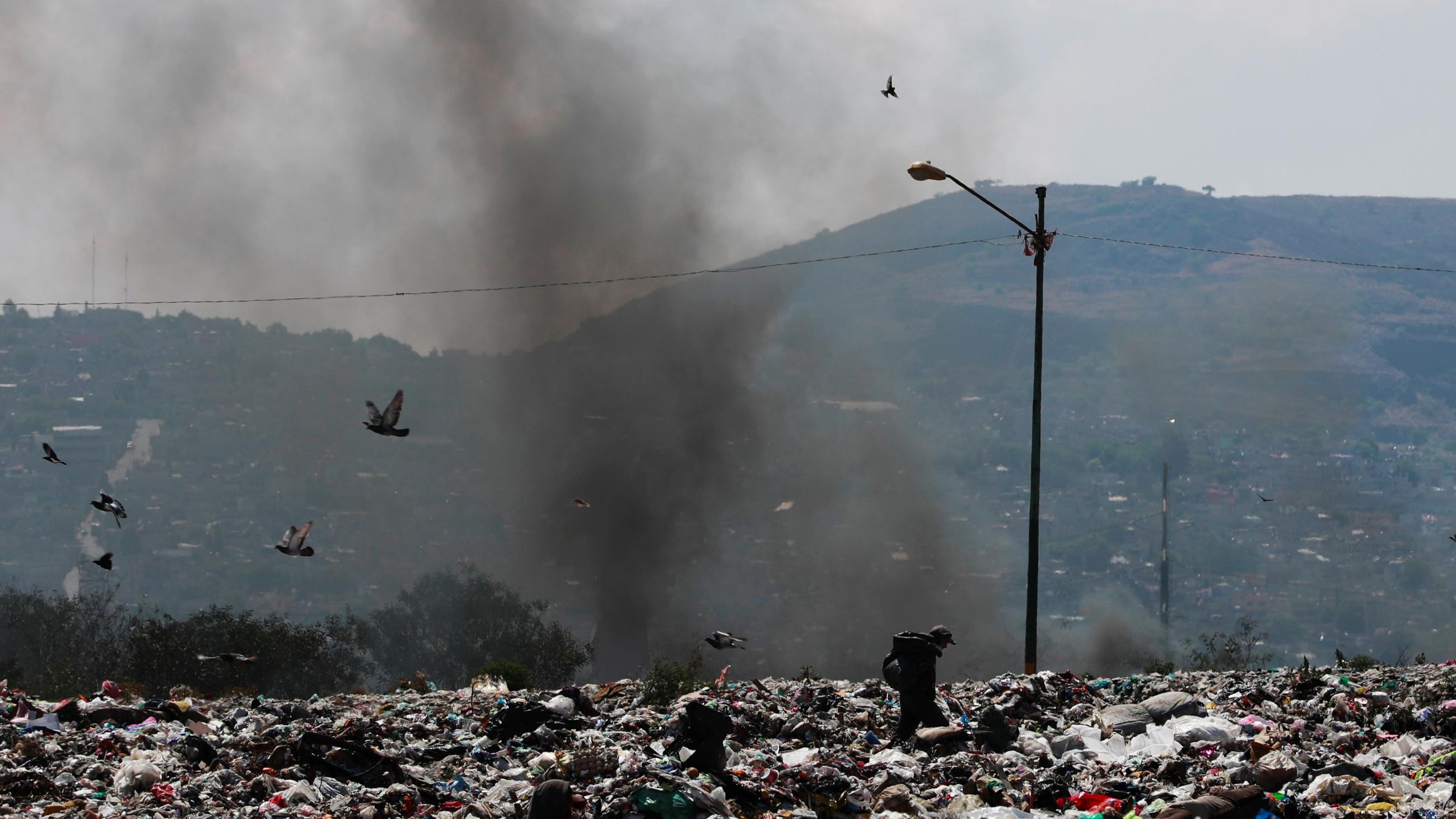 A man works on a garbage dump as black smoke rises in the background on the outskirts of the city, as the coronavirus disease (COVID-19) continues in Mexico City, Mexico, on April 27, 2020.