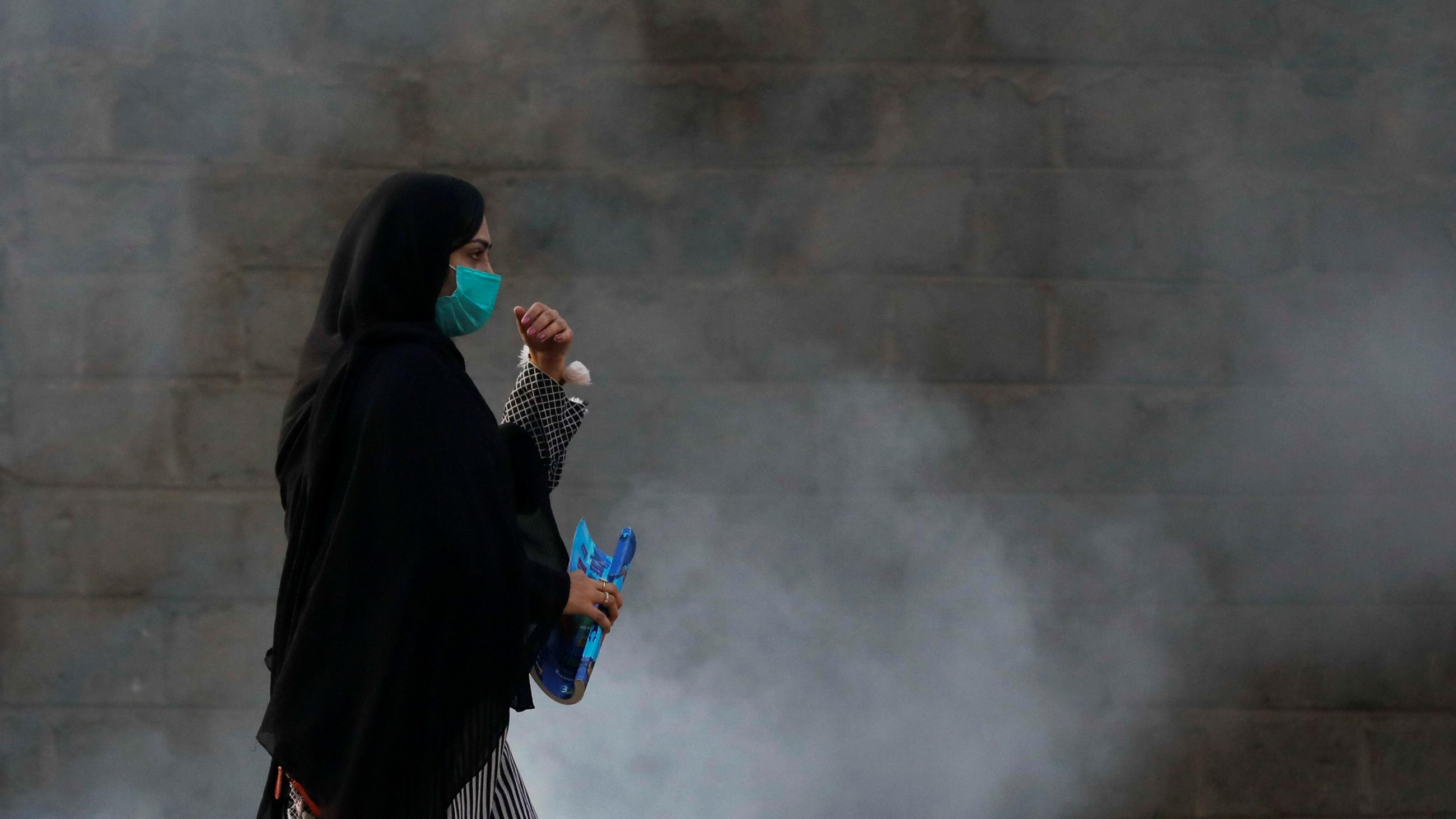 A woman wearing a protective mask walks past a cloud of smoke from a smoldering pile of rubbish along a road in Karachi, Pakistan, on October 13, 2021. 