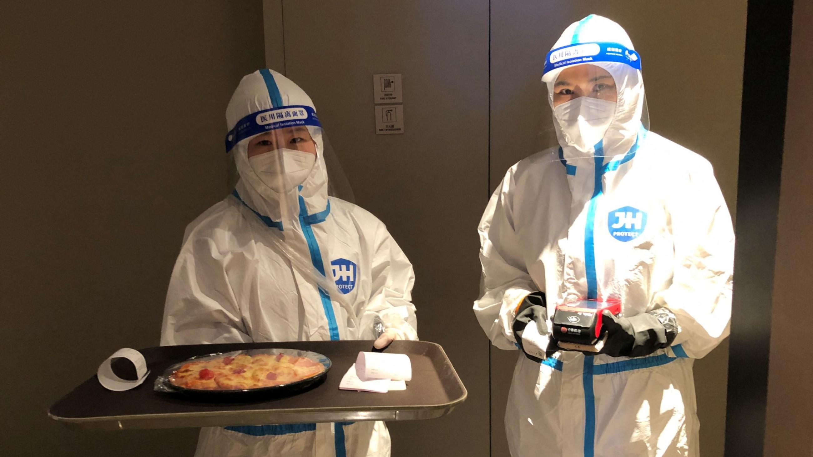 Two hotel staff wearing personal protective equipment (PPE) deliver a Margherita pizza wrapped in cling film that was ordered with room service at a hotel for journalists and officials o