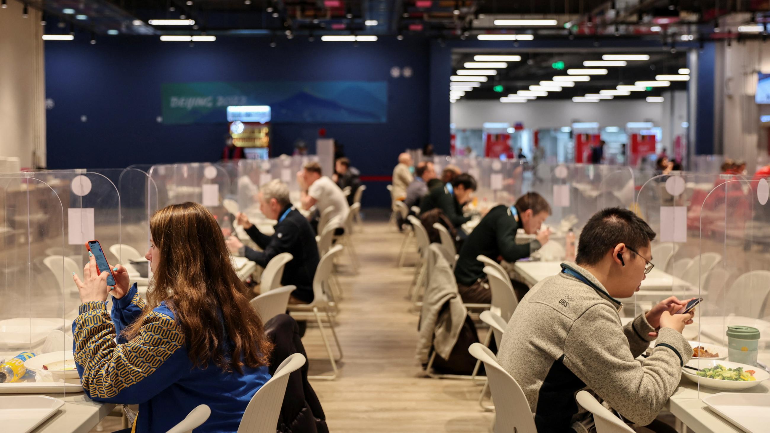 People eat between plastic barriers at the dining hall of the main media center at Beijing 2022 Winter Olympics in Beijing