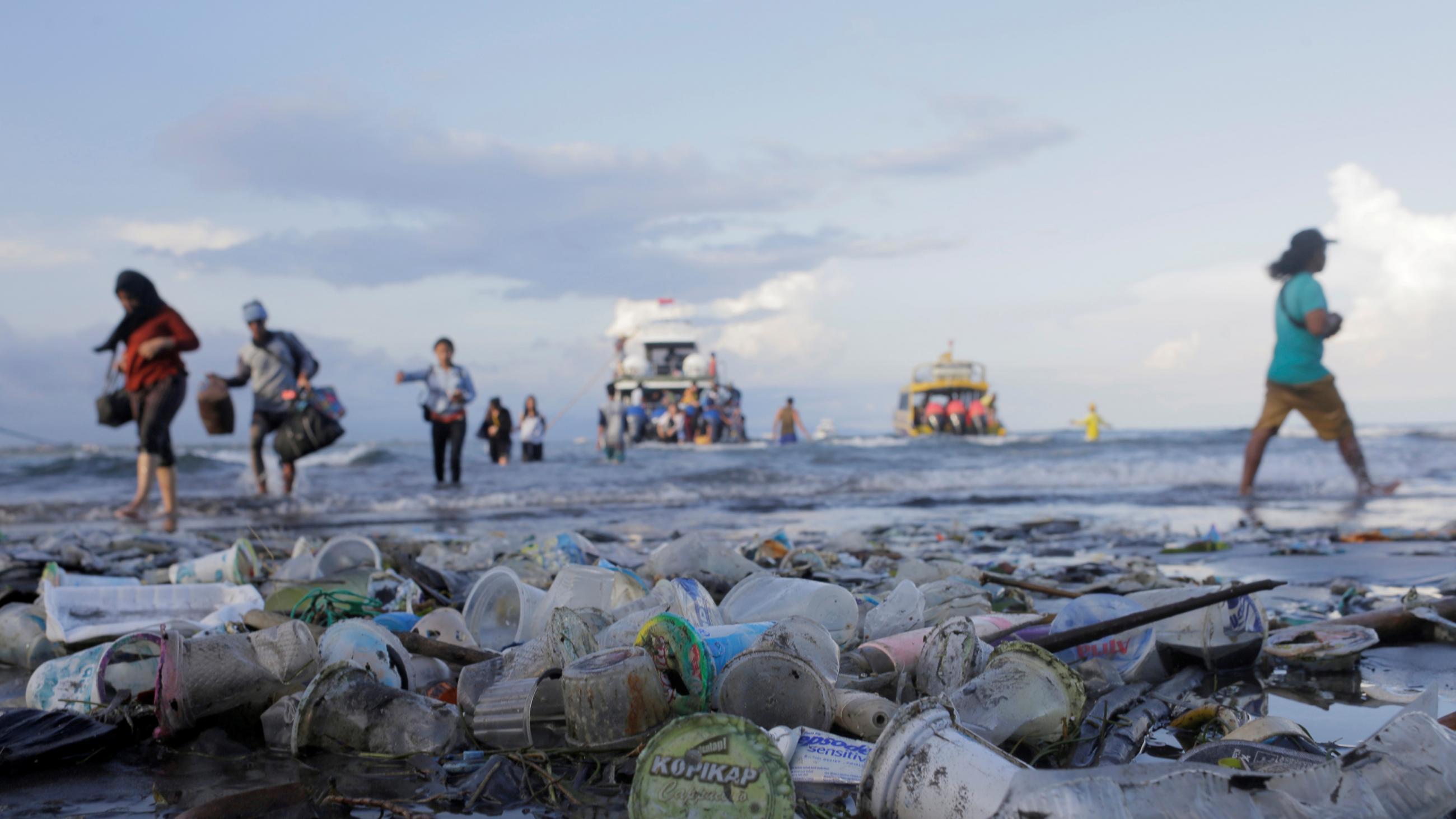 Tourists and local residents disembark from a boat onto a trash-polluted shore, in Sanur, Denpasar, Bali, Indonesia