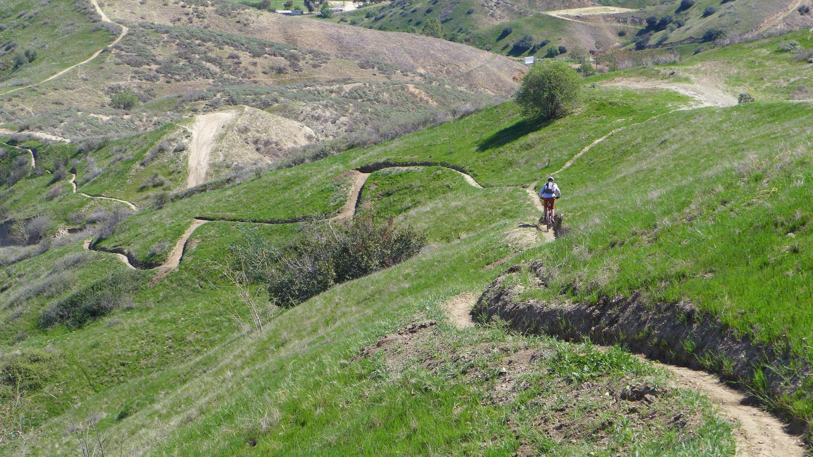 a cyclist cruises down narrow bike trail winds between green hills in a sunny valley in loma linda, california