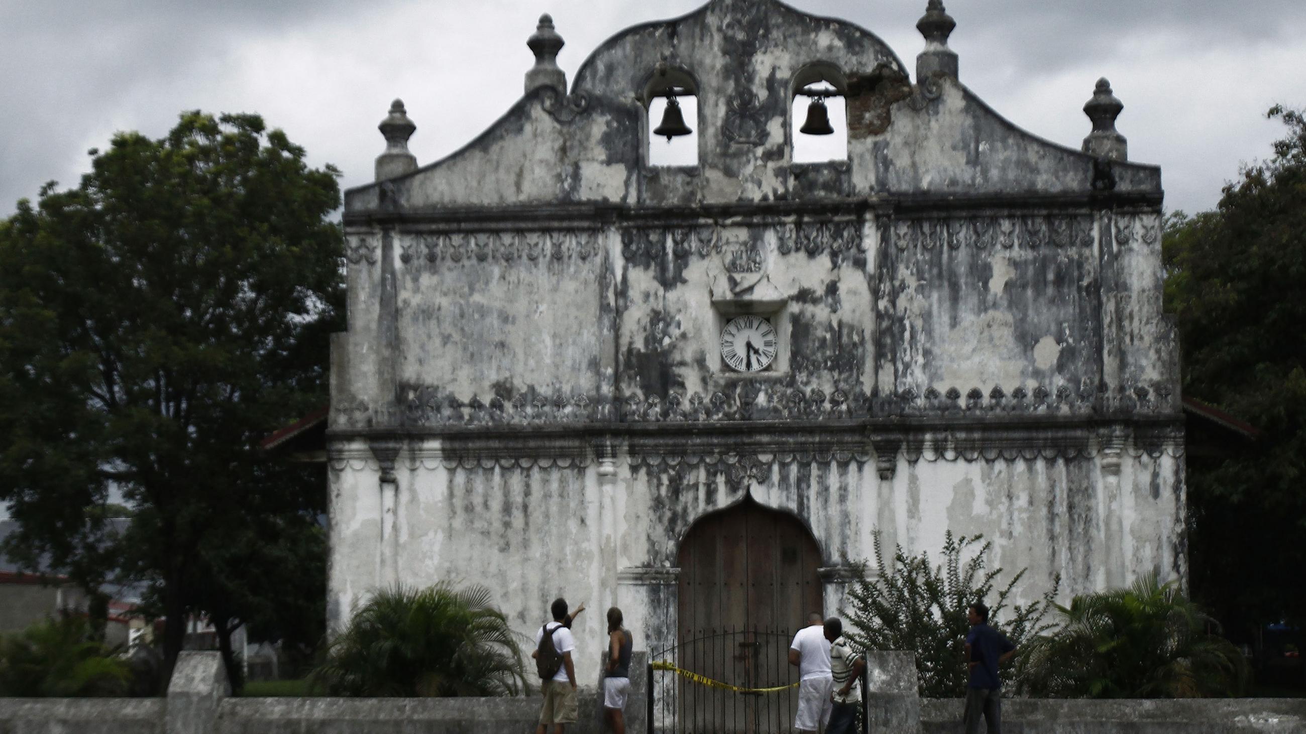 The front facade of a colonial church is pictured against the backdrop of a gray and cloudy sky