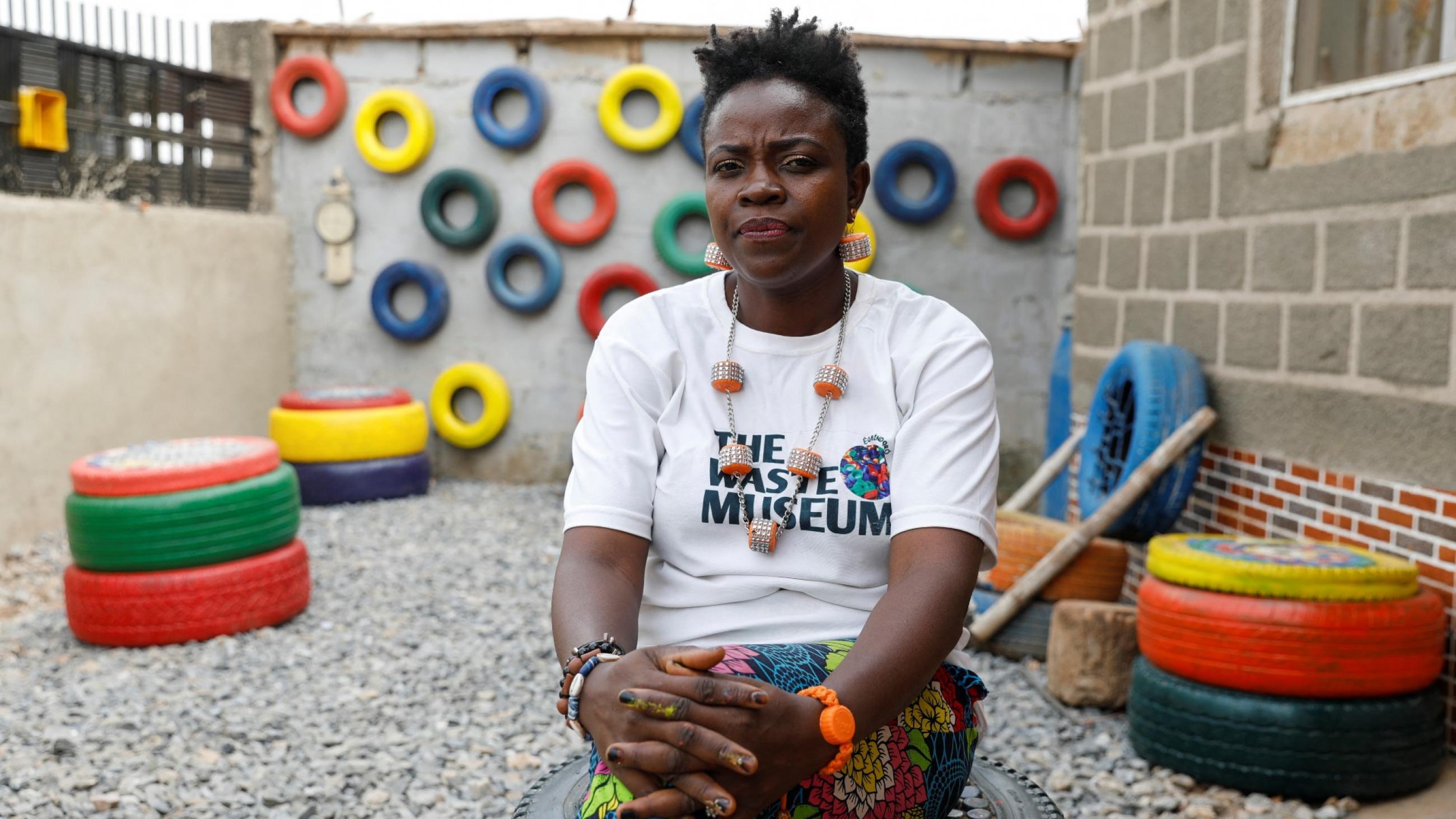Jumoke Olowookere, a black woman wearing a white t-shirt, founder of the Waste Museum is photographed sitting on a painted tire