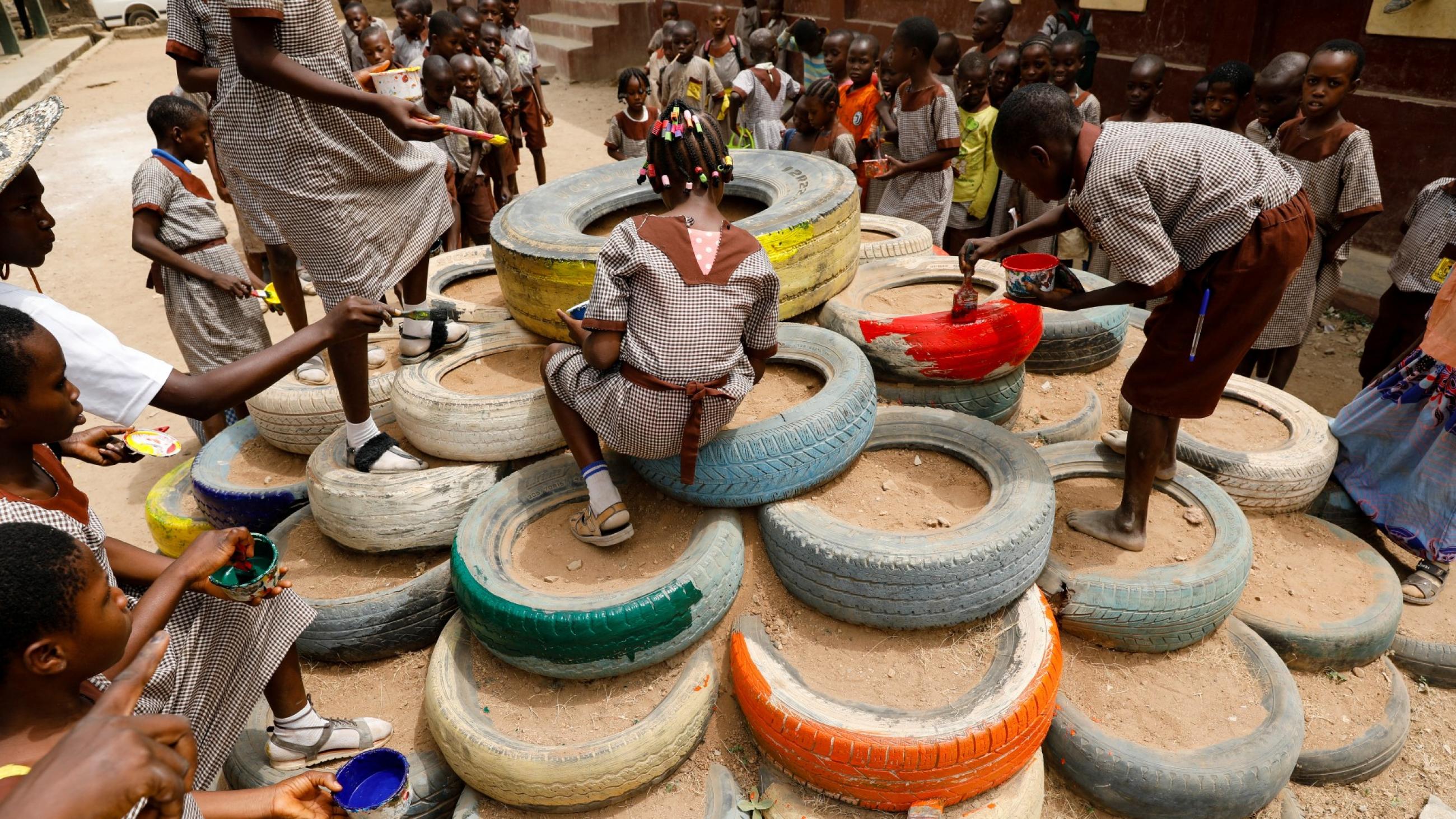 Children paint a pyramid of repurposed tires as part of a playground set up