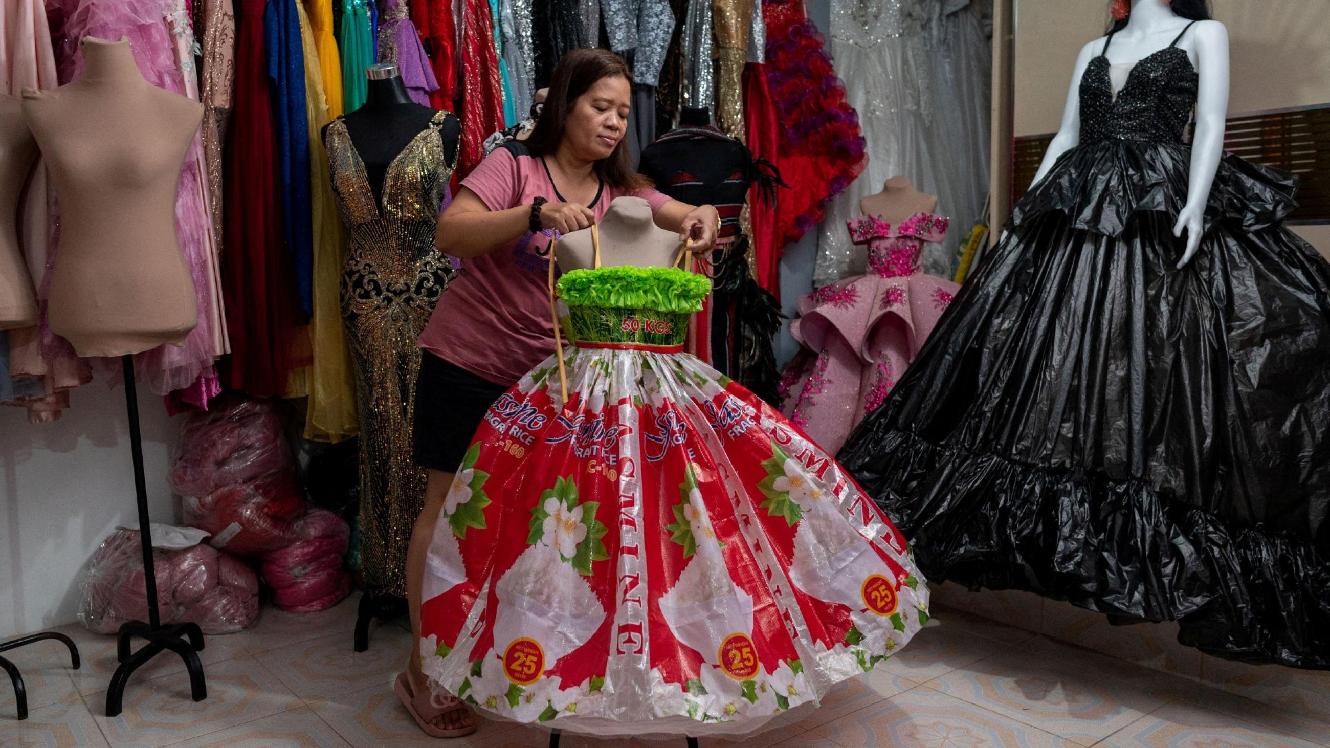 A shopkeeper arranges a pink and green formal dress made out of fabric  from recycled bottles