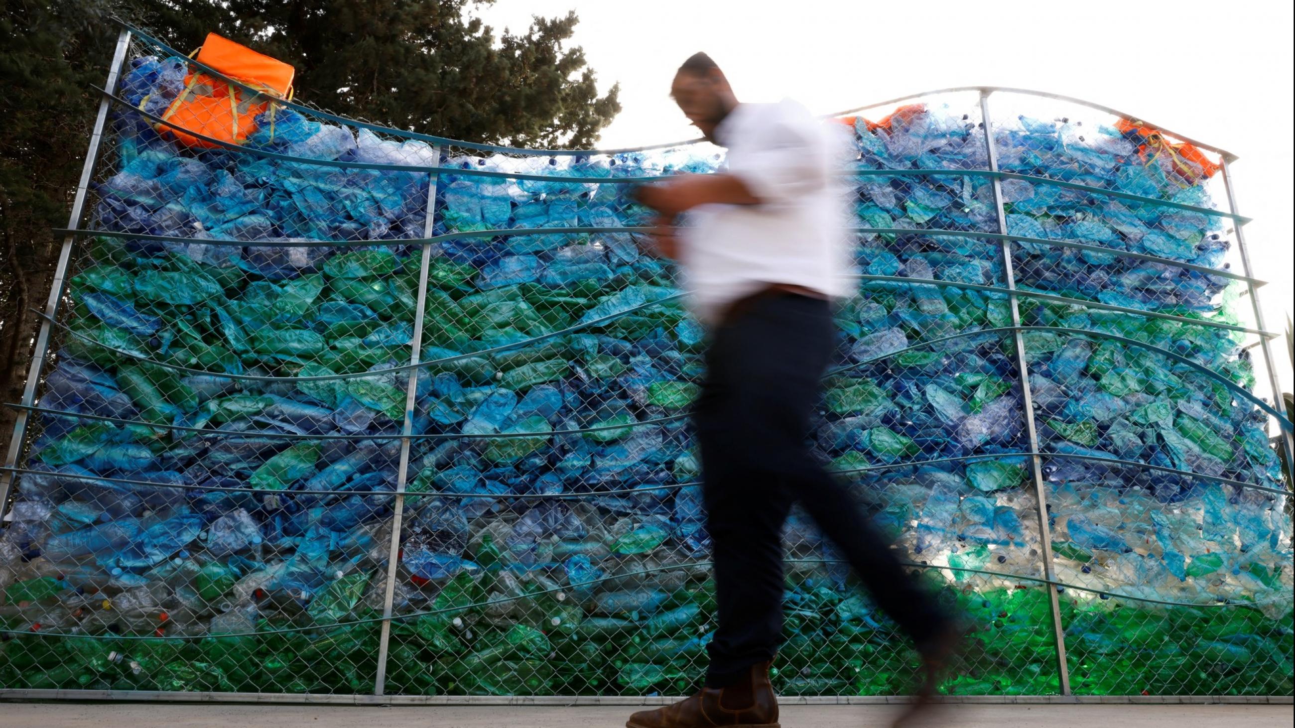 a priest, captured mid-step, is seen blurred against a crisp backdrop of repurposed, blue plastic bottles