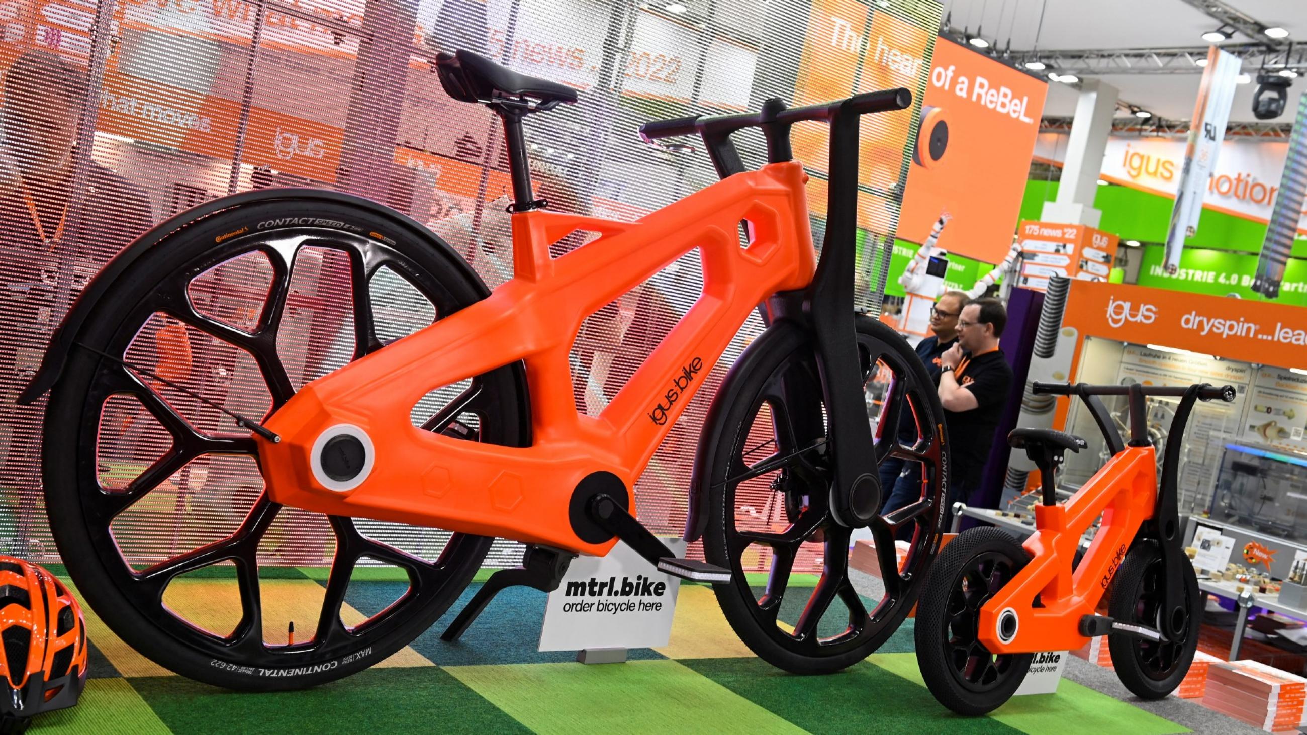 Two bright orange bicycles with black wheels are photographed on astroturf at an exhibition in Hanover, Germany
