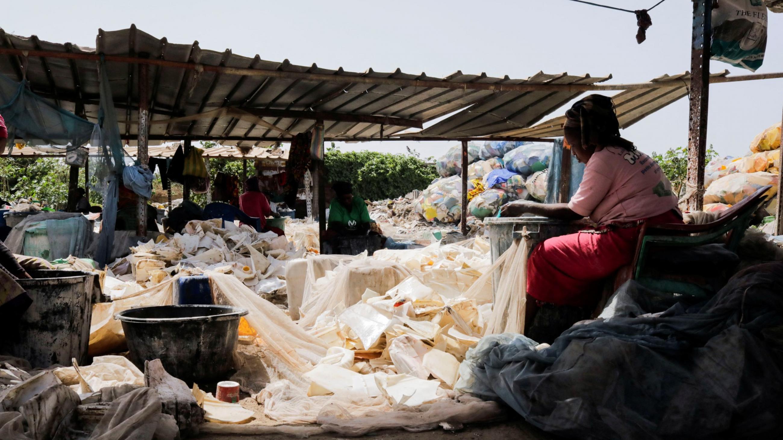 A woman sits with her back facing the camera as she washes plastic waste outside a landfill in Dakar, Senegal