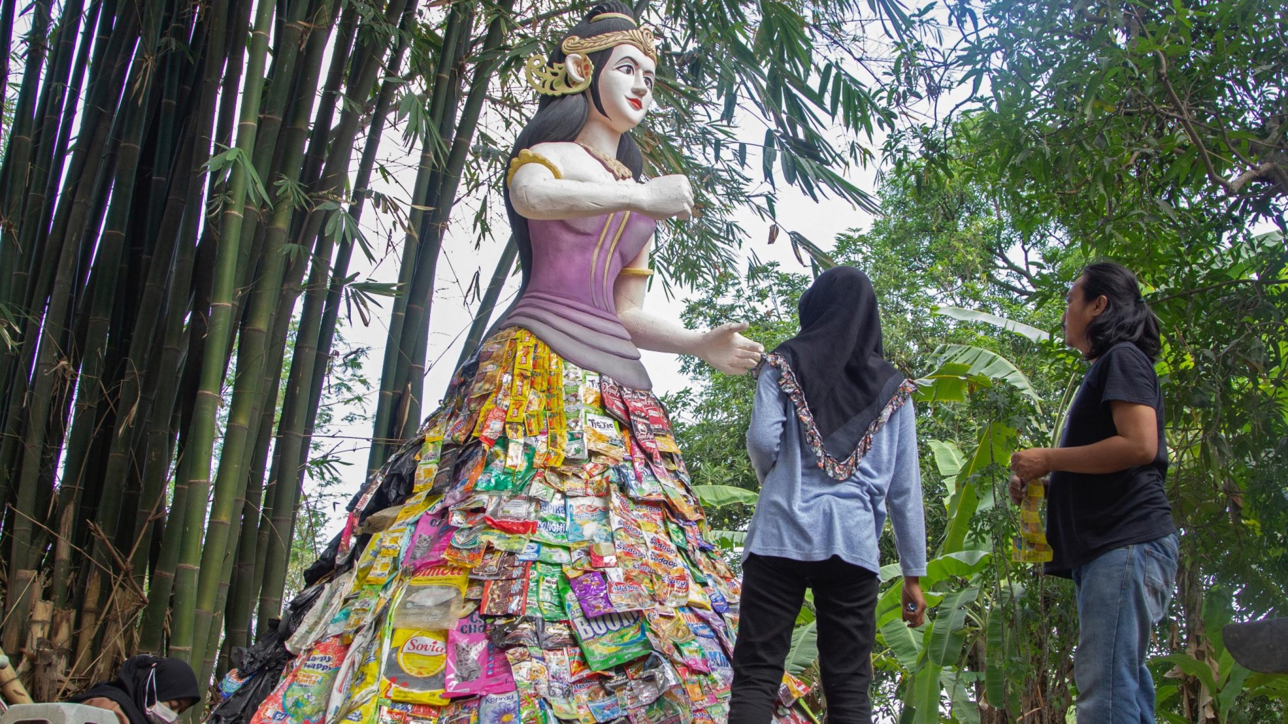 a male and female bystander look at a mock-up of the Indonesian goddess, Sri, that had been constructed from repurposed plastic waste