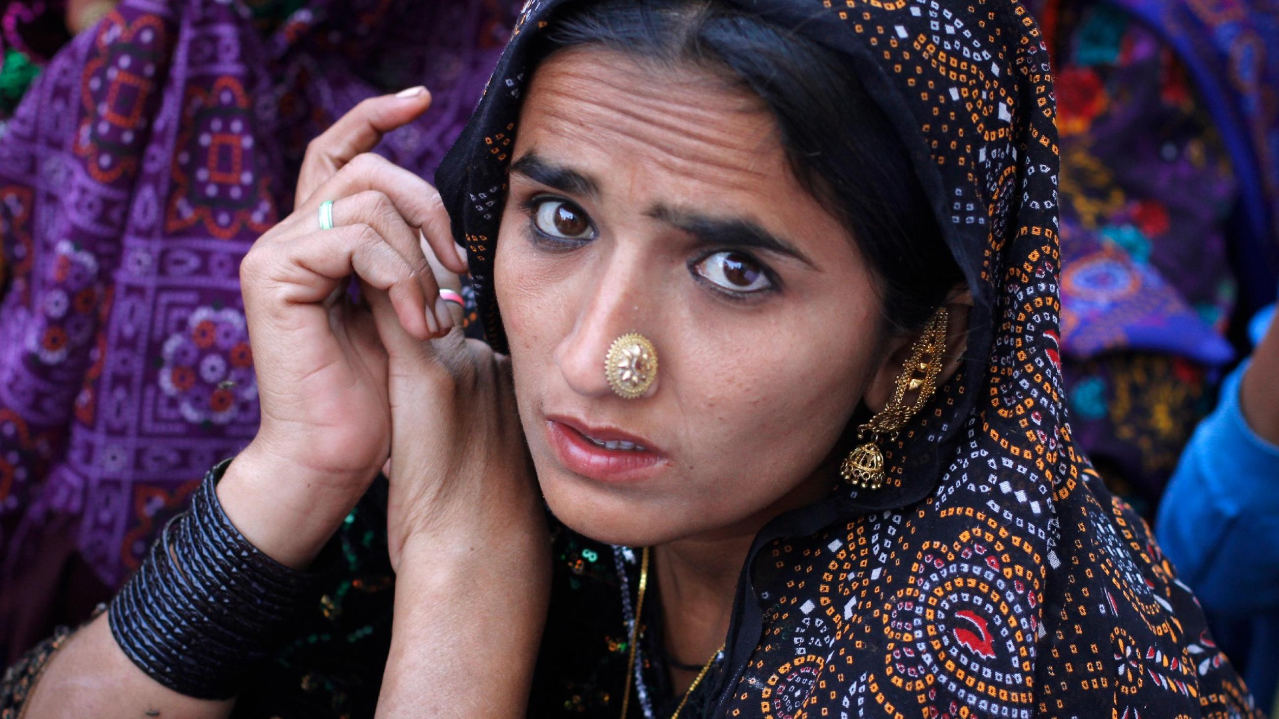 a portrait of young woman with black eyeliner and a large, gold, nose ring wearing a heavily embellished purple head scarf