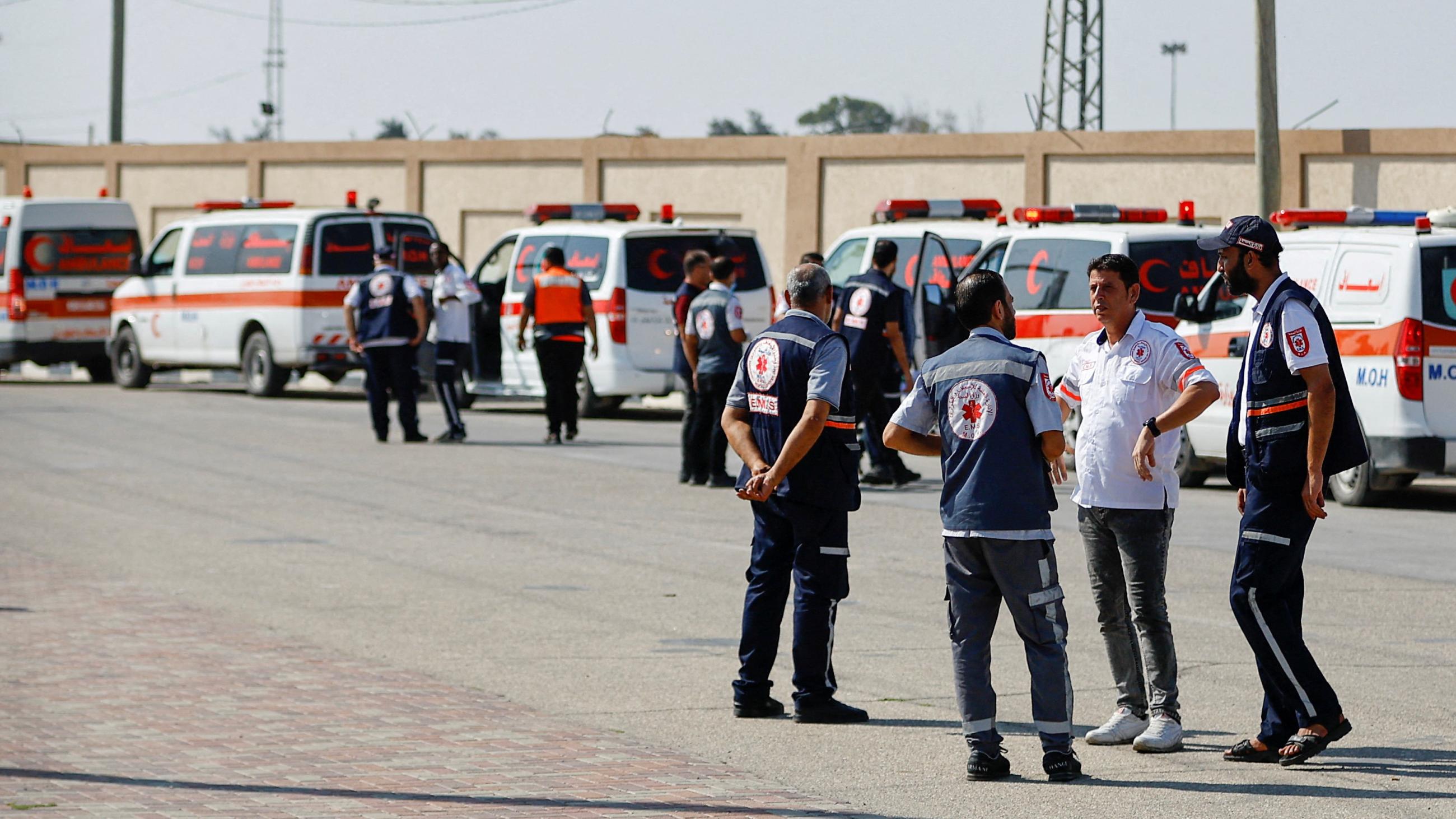 A group of men is seen standing beside a line of ambulances 