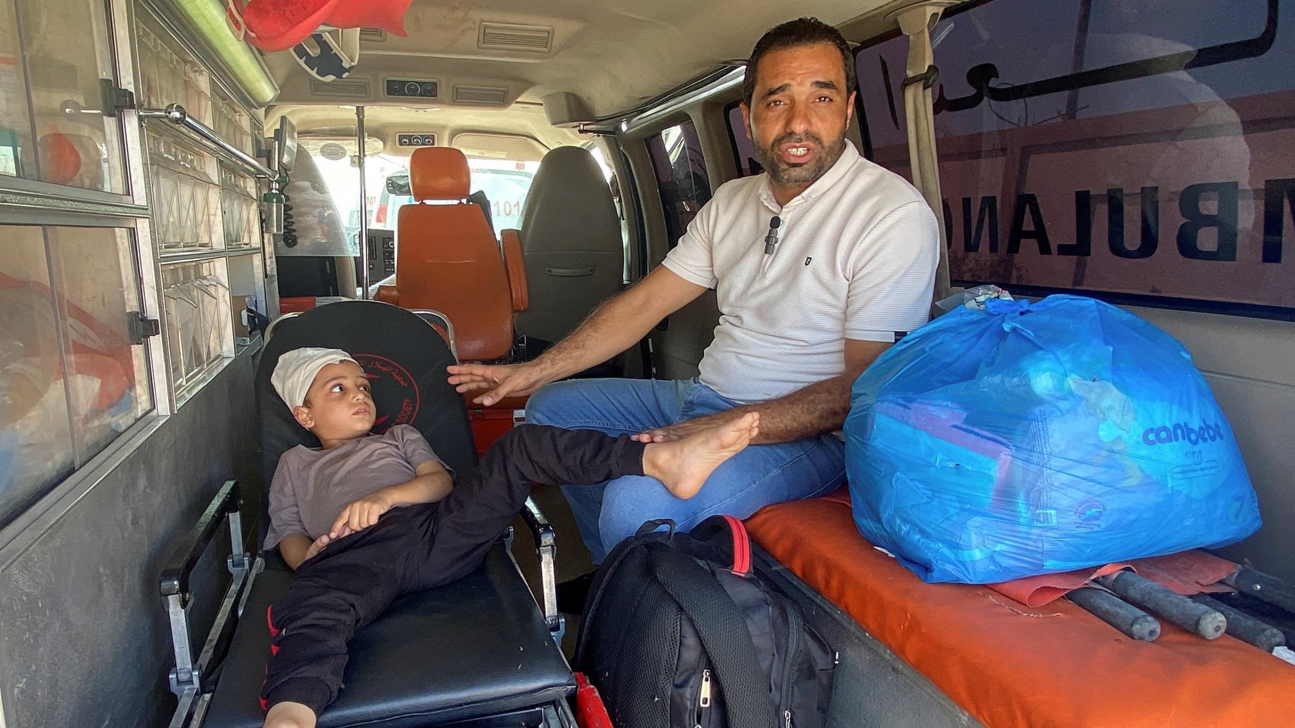 a boy sits on a gurney with a man watching over him in an ambulance.